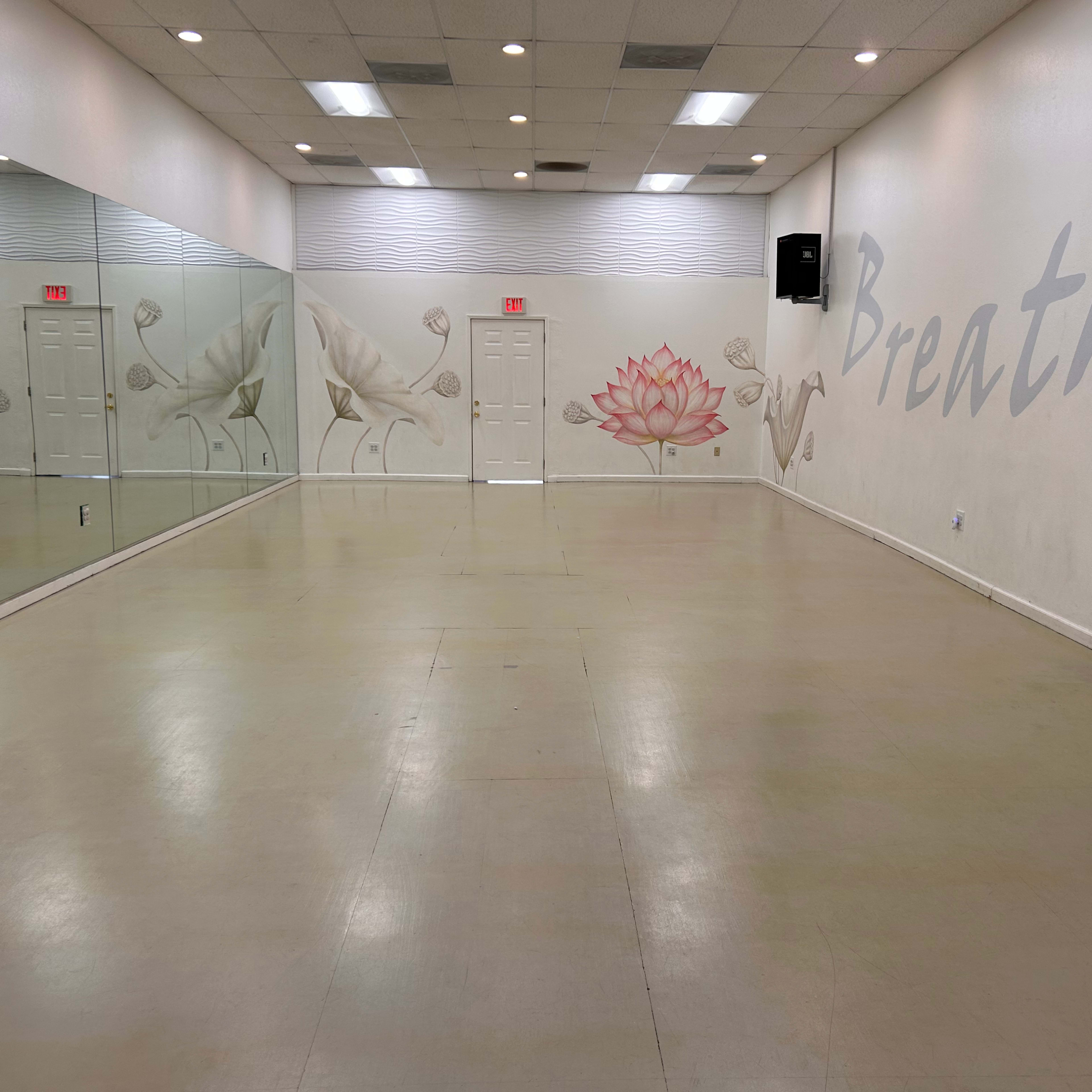 A spacious, empty studio with mirrored walls and a large mural of flowers along one side.