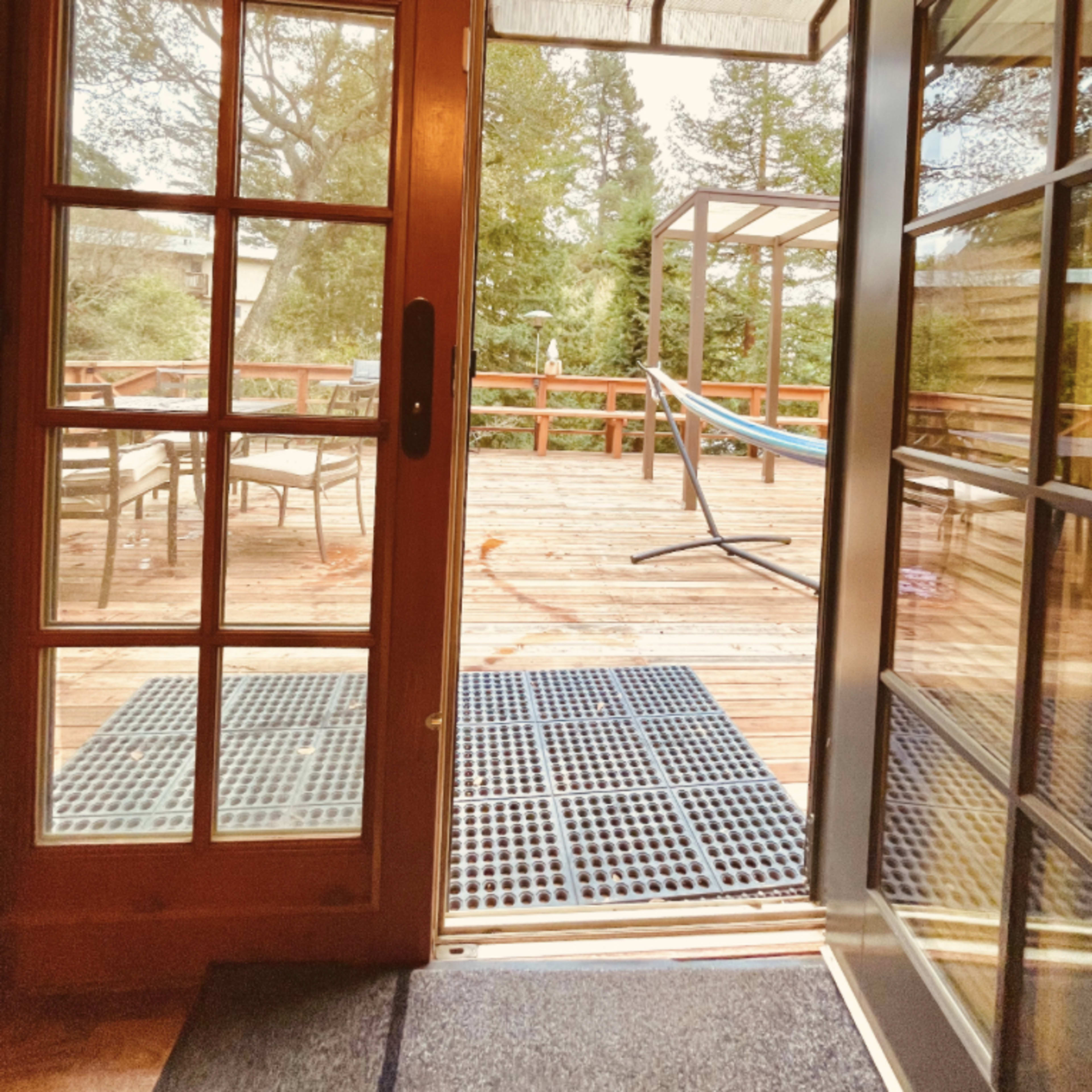 A wooden door opens to a deck area with a hammock, outdoor seating, and surrounding trees.