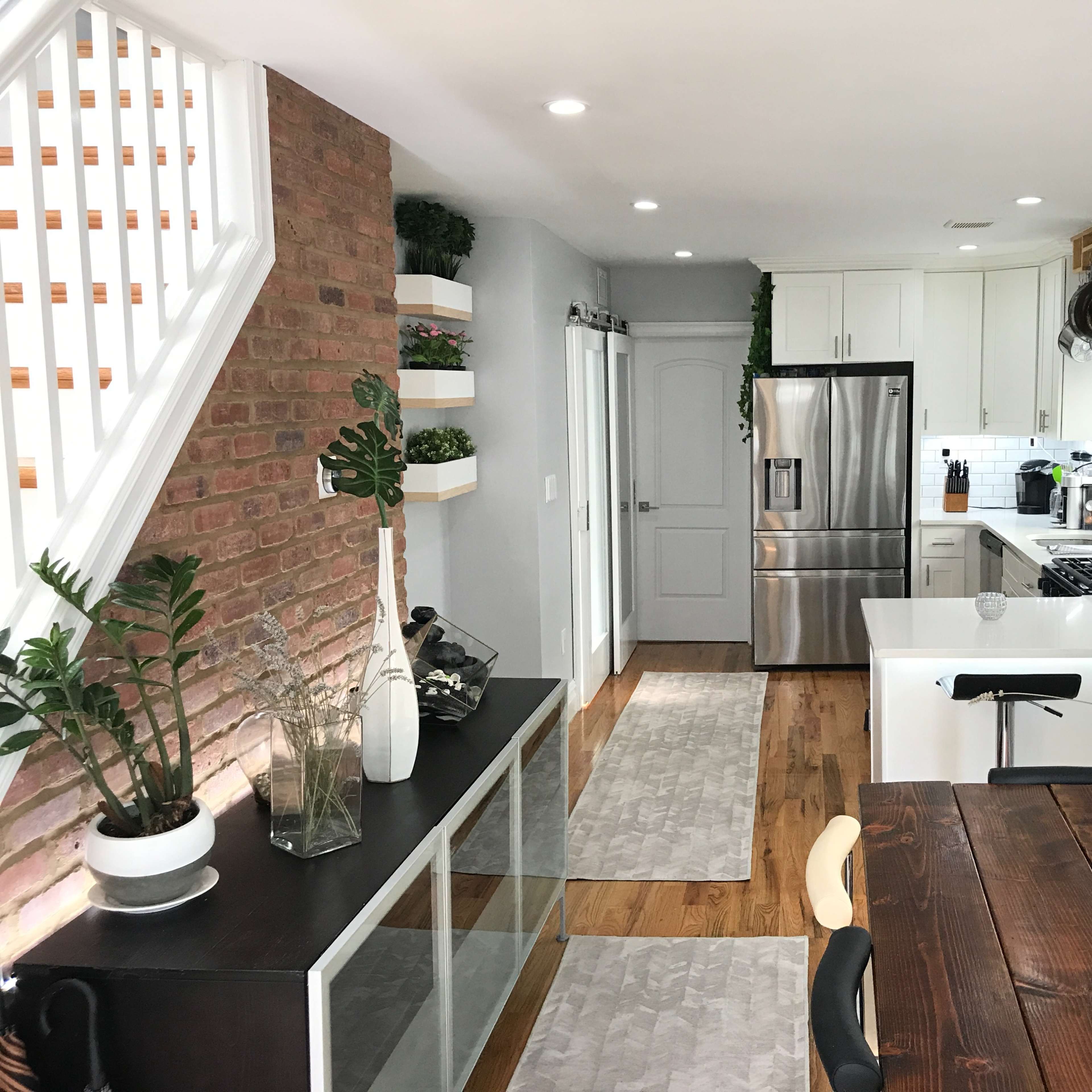 A modern kitchen and dining area featuring a brick accent wall, stainless steel appliances, and a wooden dining table.