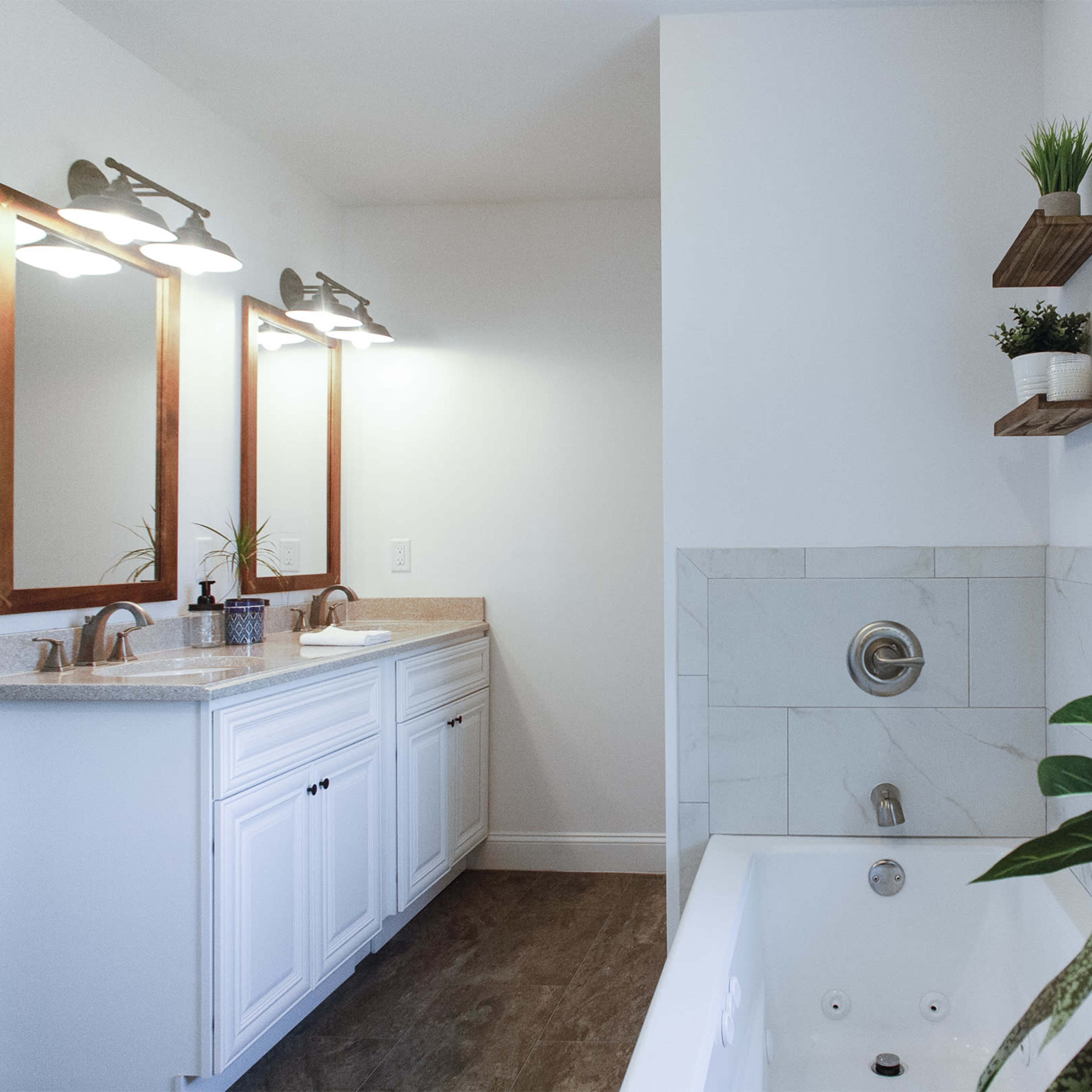 A modern bathroom with dual sinks, a bathtub, and a plant near the window.