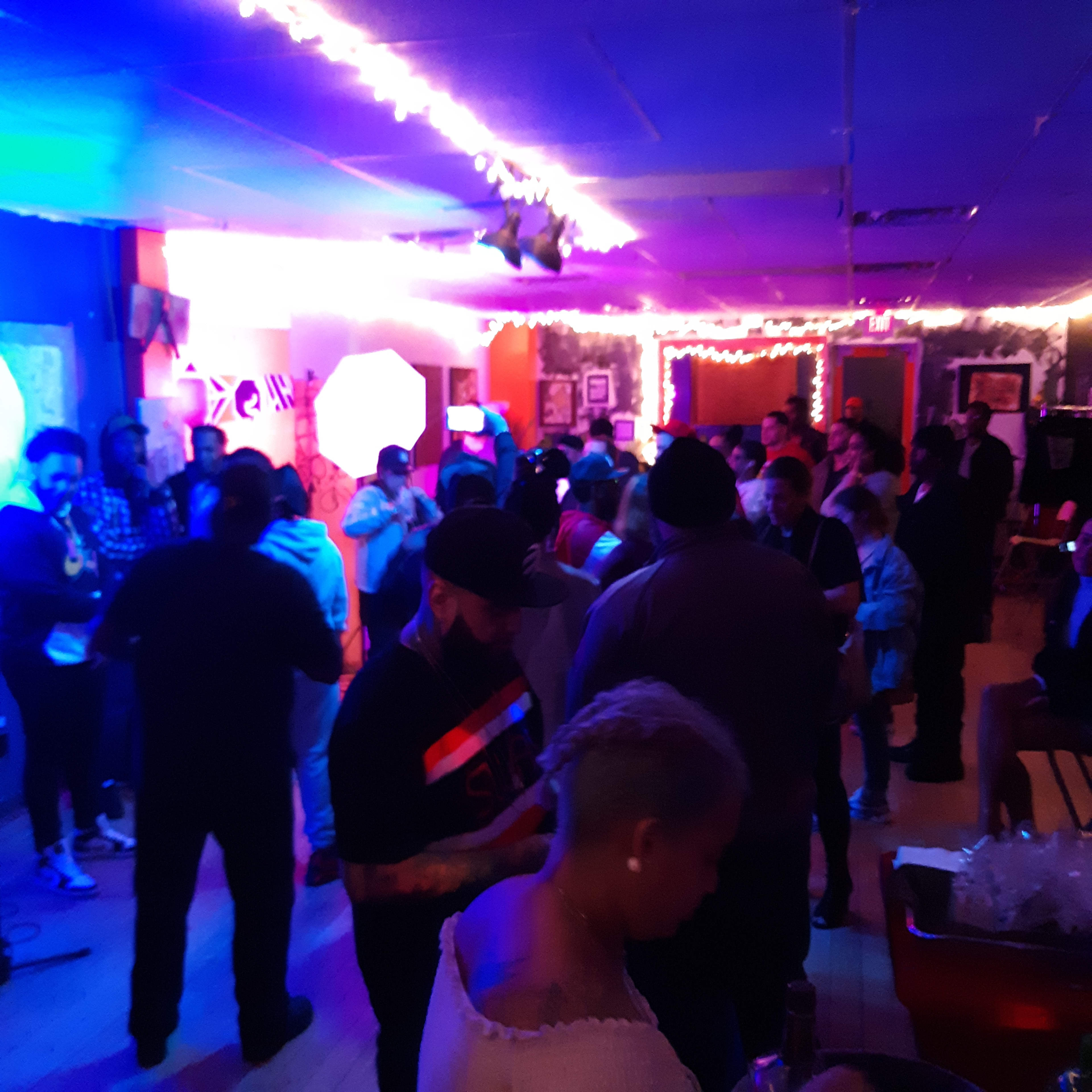 A crowded room filled with people socializing under colorful lights, with some individuals holding up their phones.