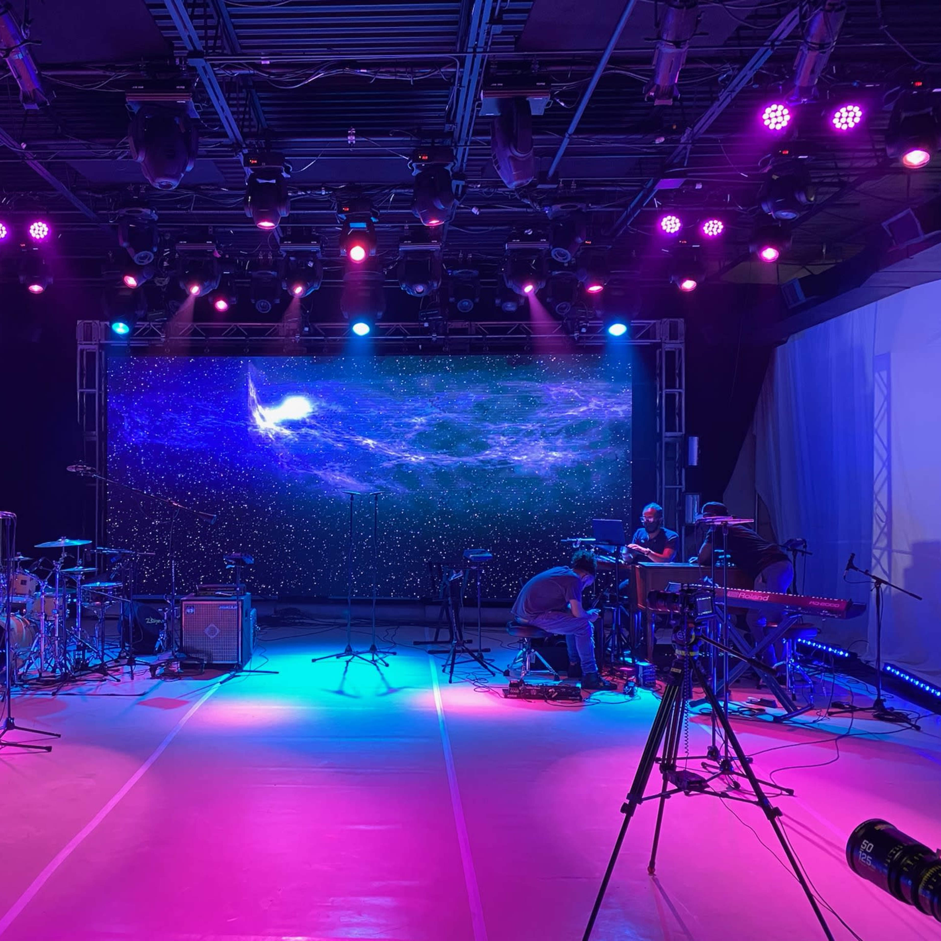 A stage set up for a performance, featuring musical instruments, microphones, and a large backdrop with a cosmic-themed projection.