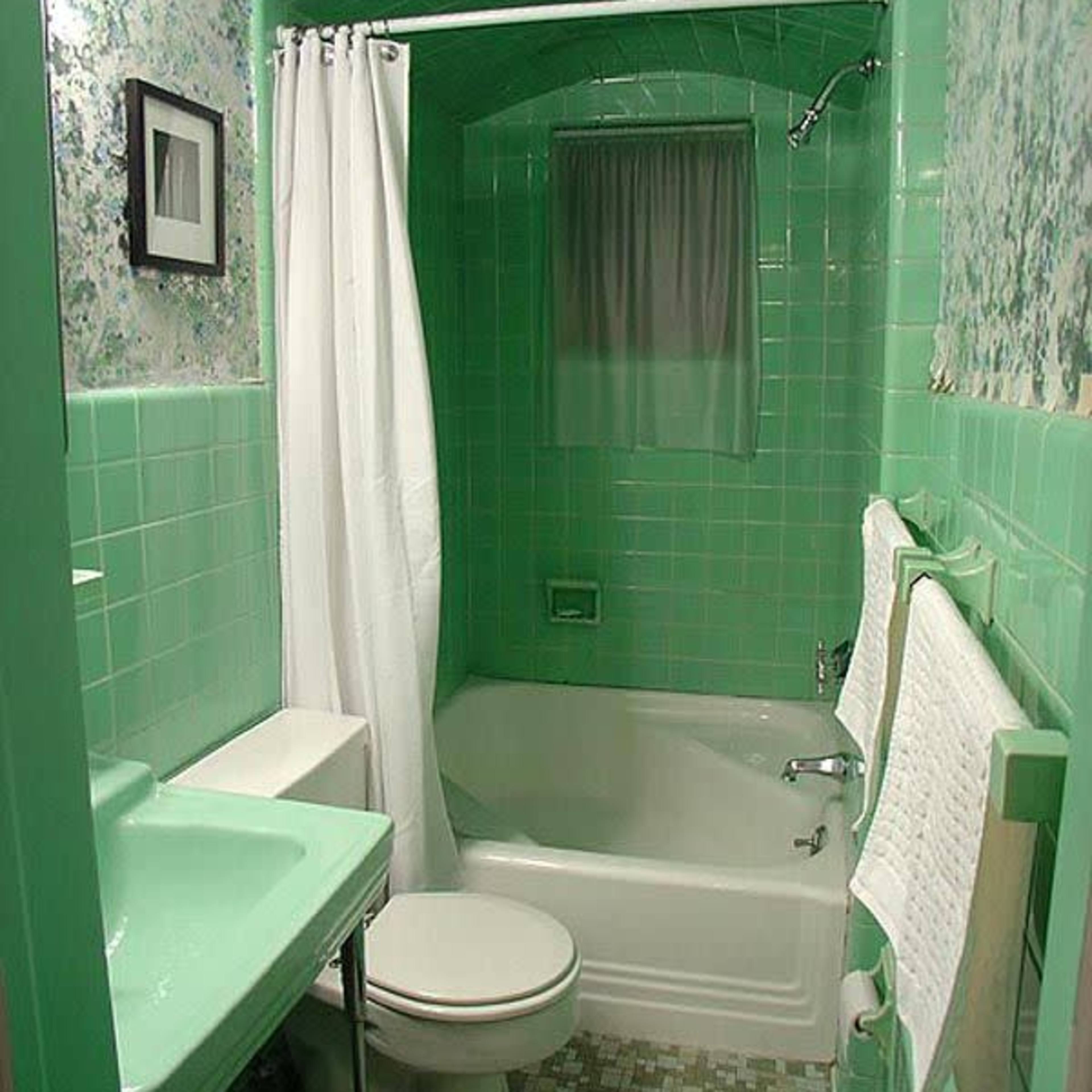 A small bathroom featuring green tiles, a bathtub with a shower, a toilet, and a sink with a mirror above it.