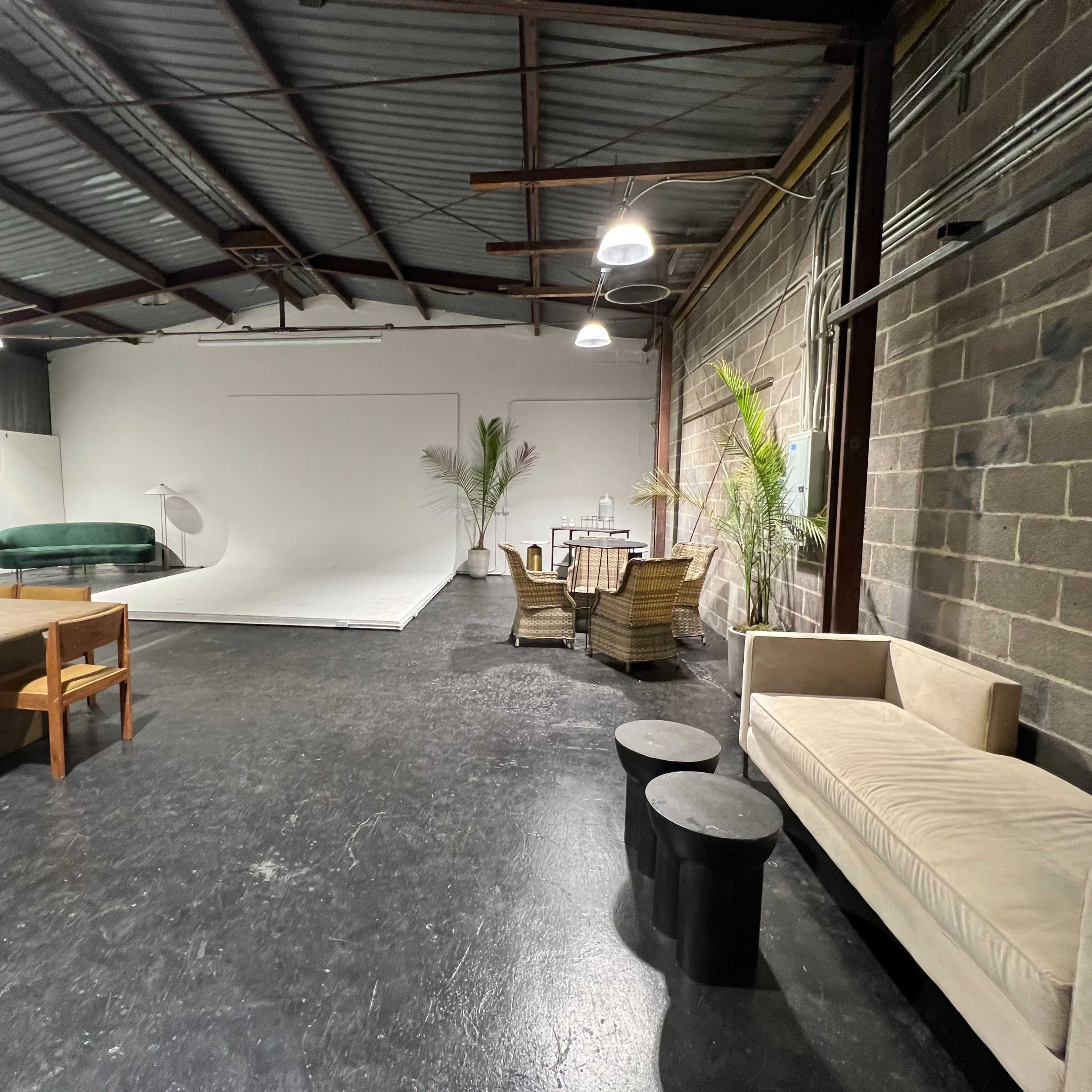 An industrial-style studio space with a seating area, a dining table, and a large white backdrop.