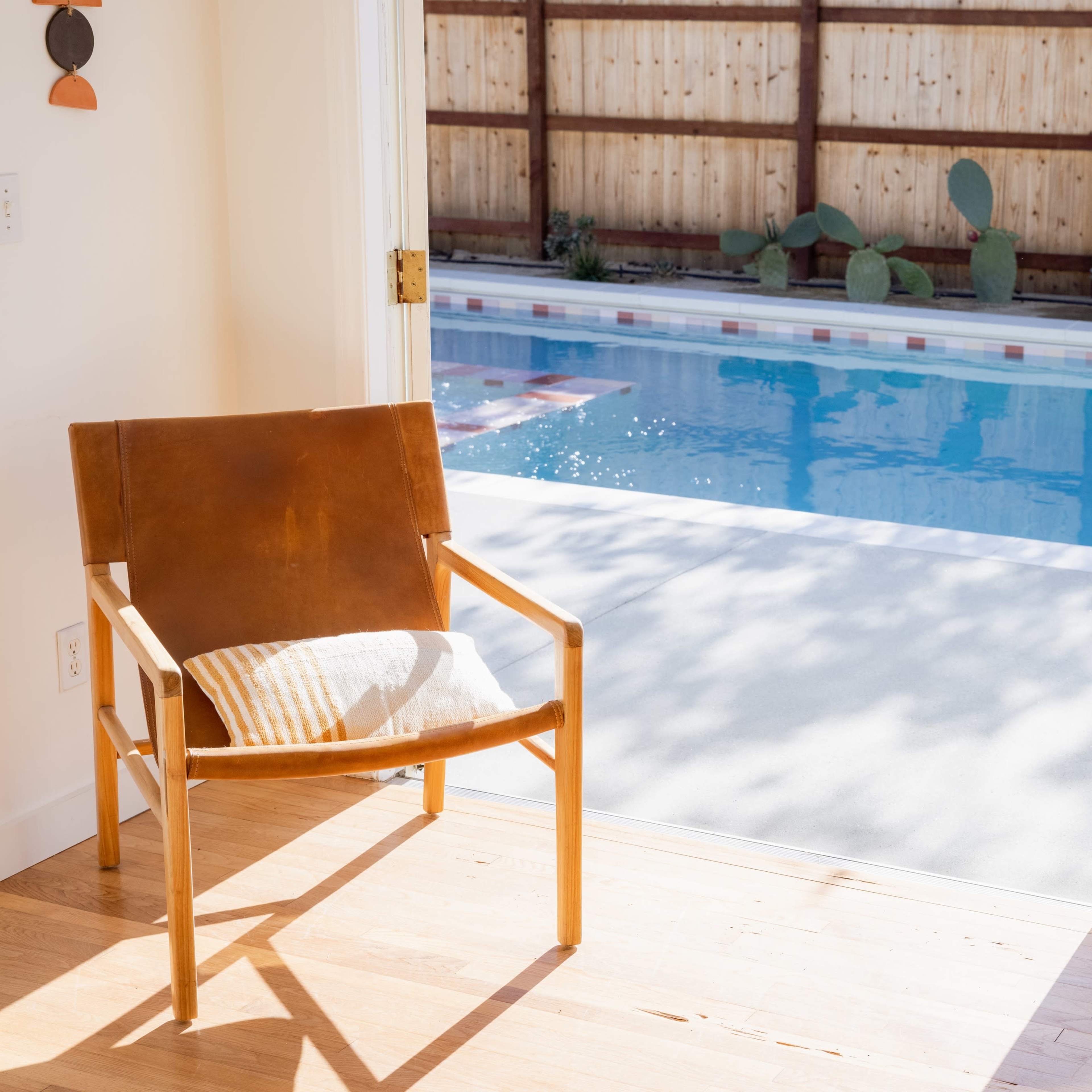A wooden chair with a cushion faces a swimming pool visible through an open doorway.
