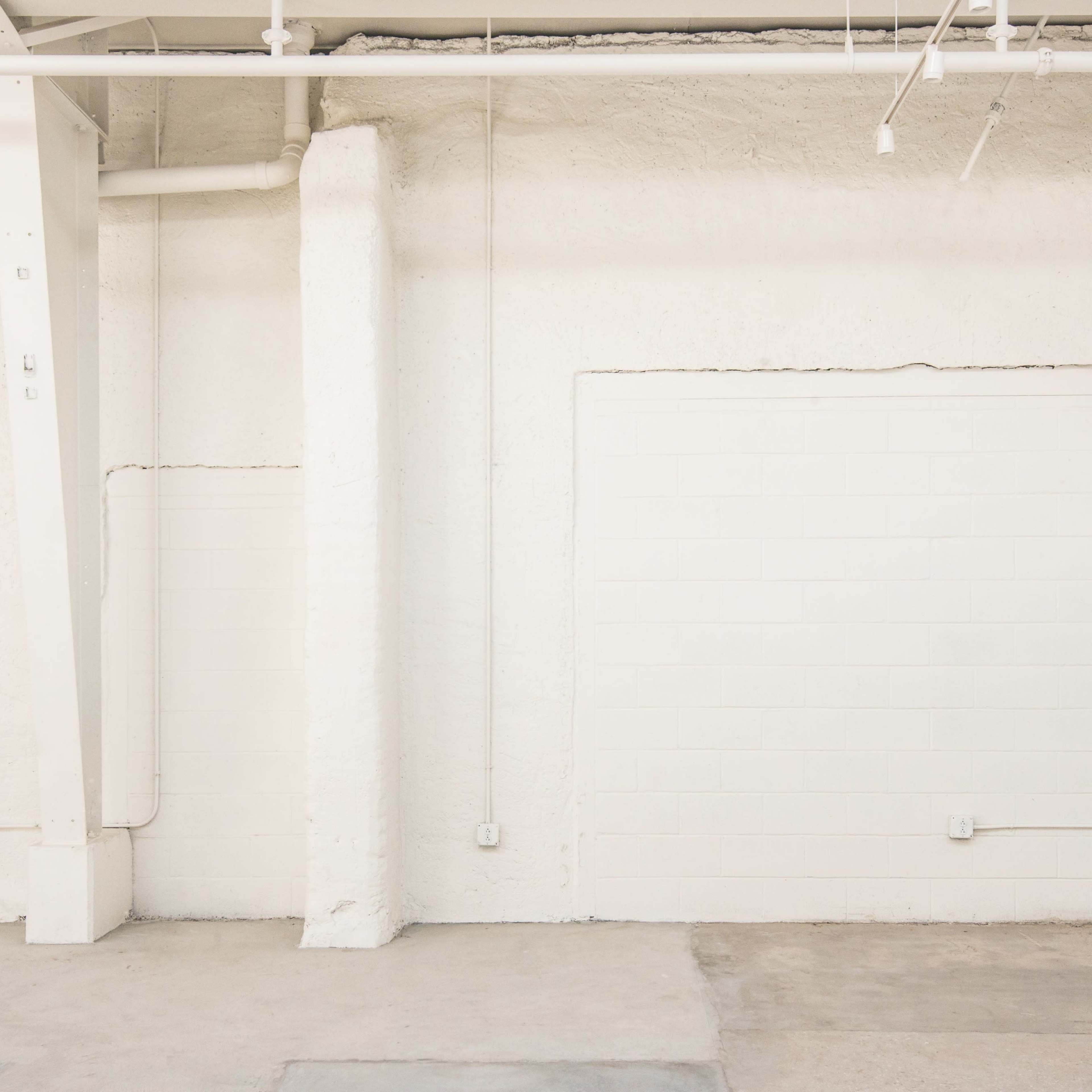 An empty room with white walls, concrete flooring, and exposed industrial features.