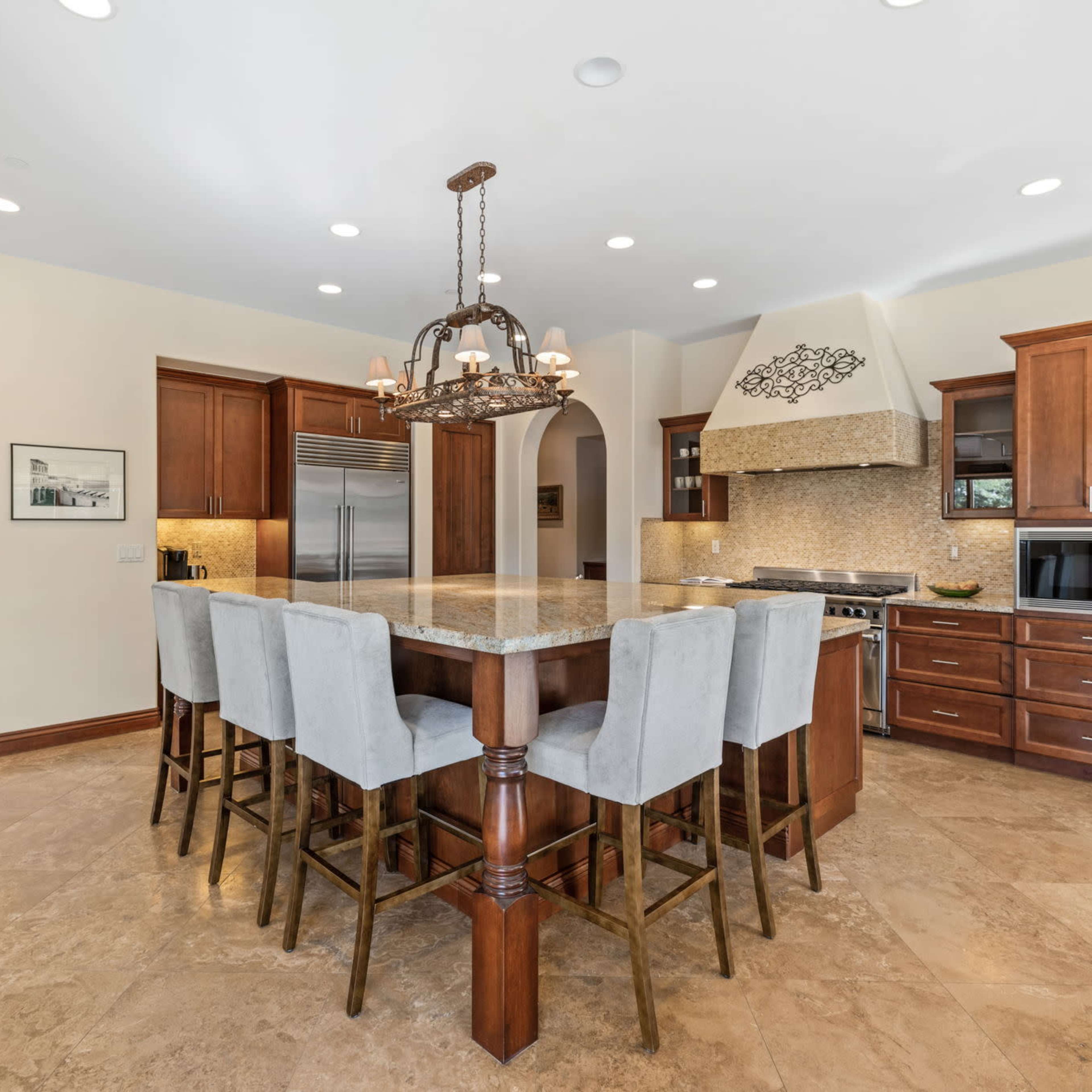 The kitchen features a large granite island with eight upholstered bar stools, wooden cabinetry, and a tile backsplash.