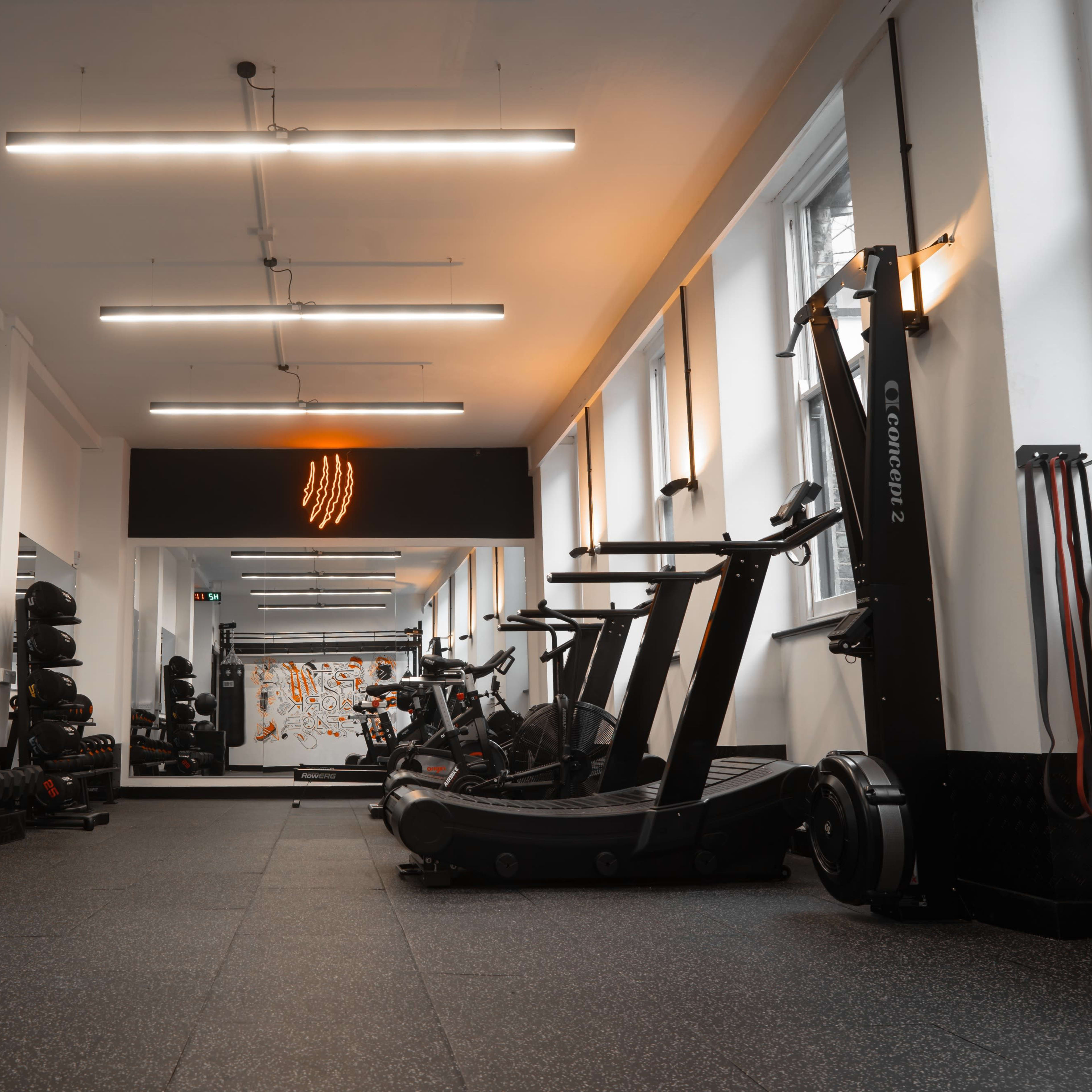 A modern gym with various fitness equipment against a backdrop of bright lighting and large mirrors.