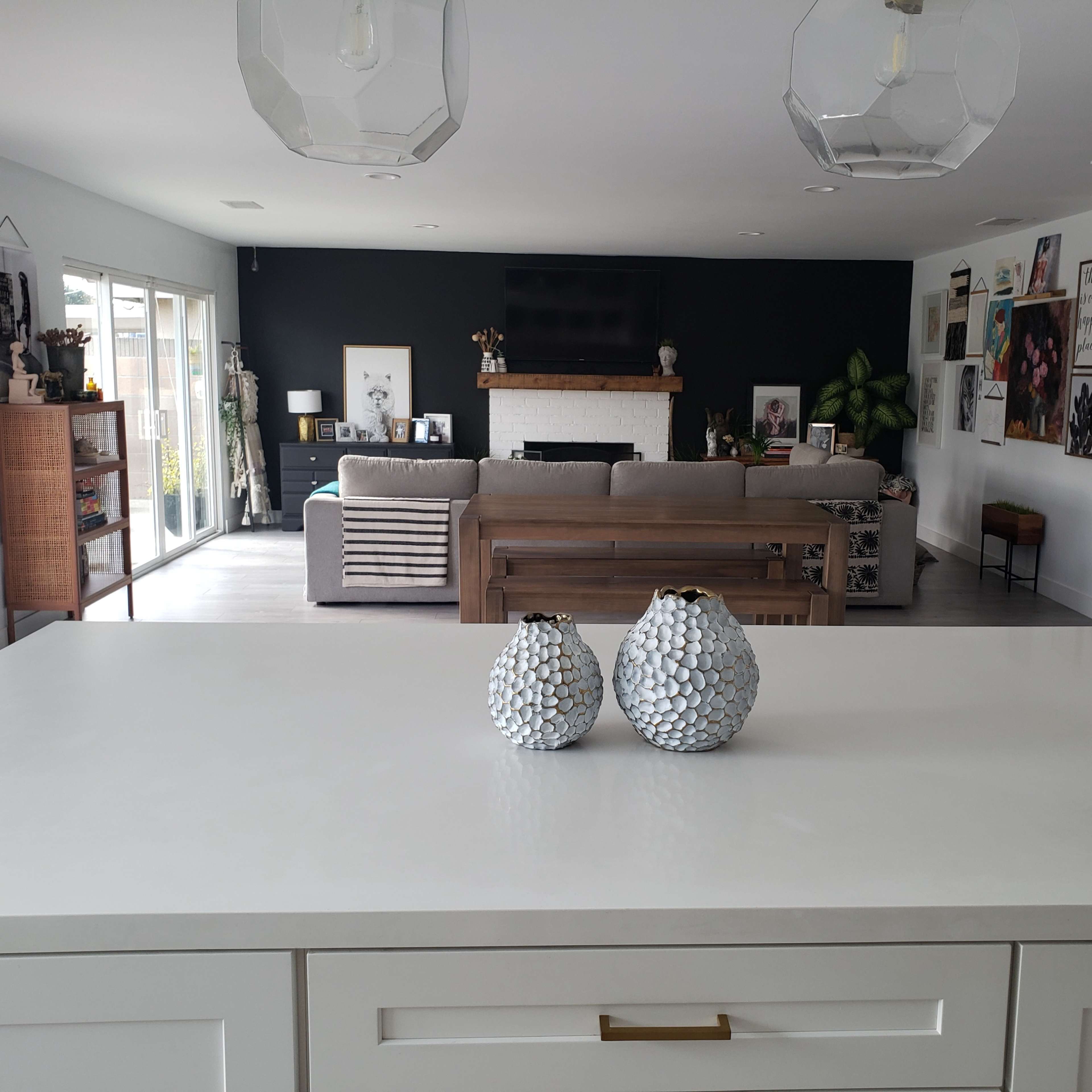A modern living space features a kitchen island with decorative vases in the foreground and a cozy seating area with artwork on the walls in the background.