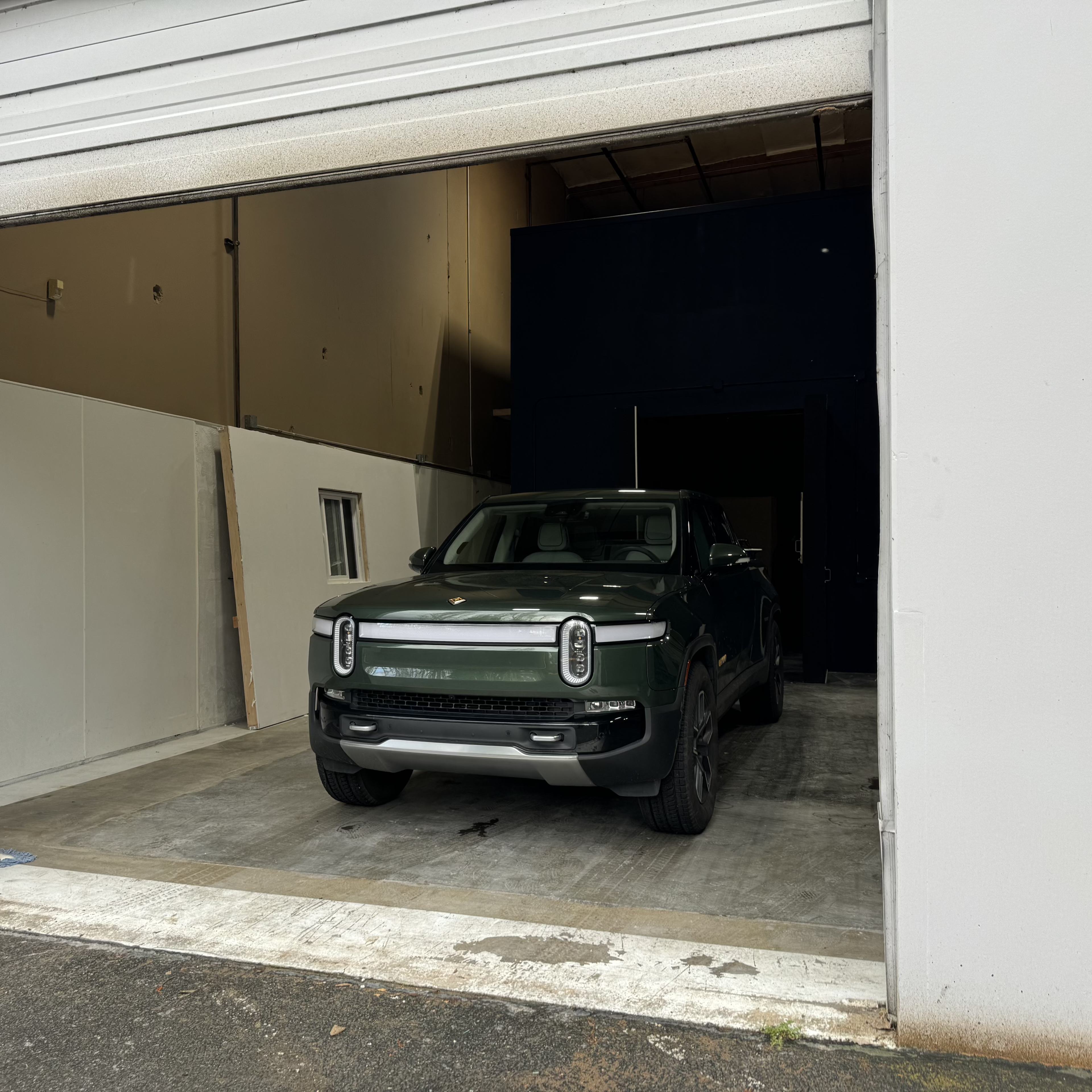 A green vehicle is parked inside a garage with an open door.