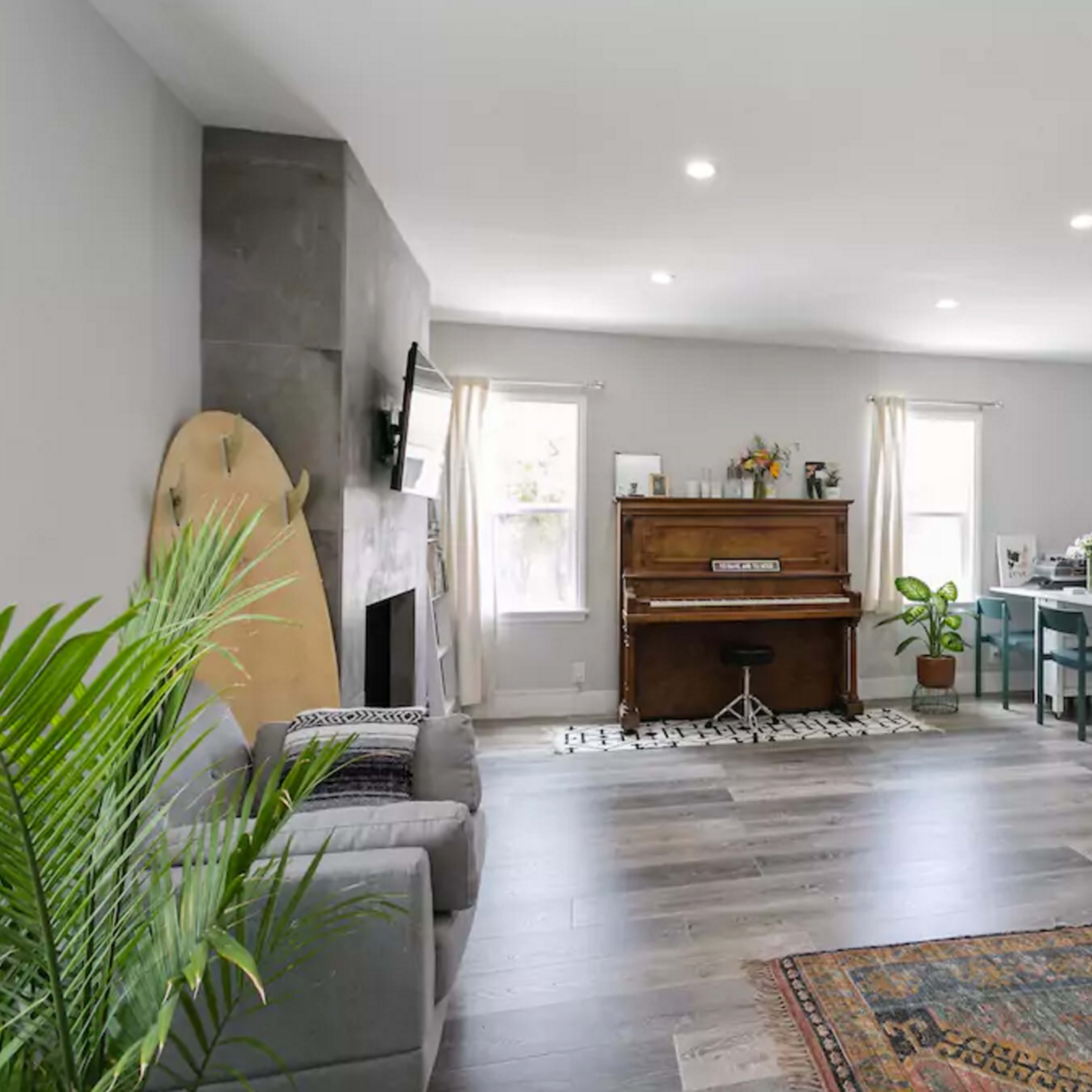 A spacious living area with a piano, a dining table, and a couch, featuring light-colored walls and wooden flooring.