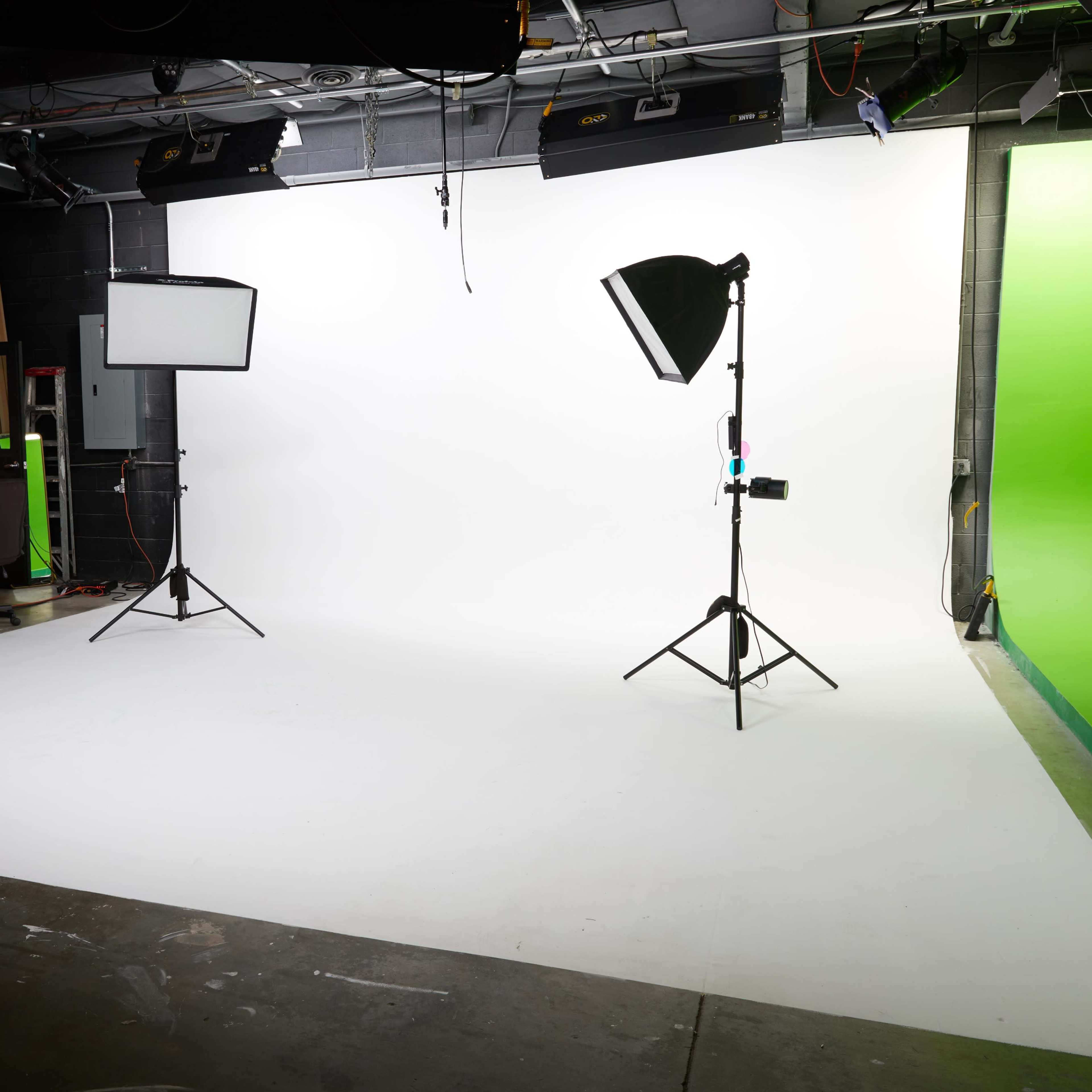 A photography studio with a white backdrop, two lights on stands, and a green screen in the corner.