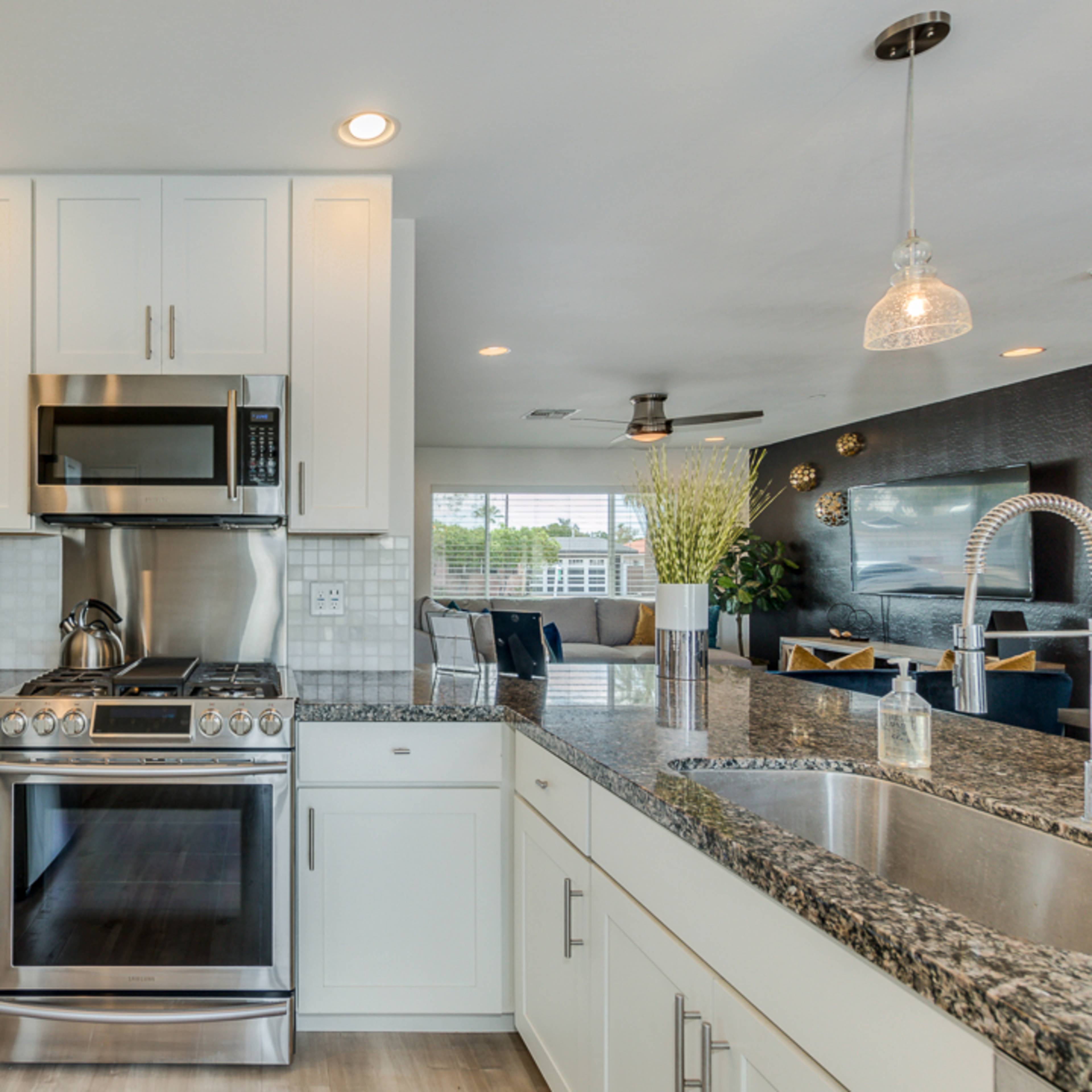 A modern kitchen with white cabinets, a stainless steel stove and microwave, and a granite countertop.