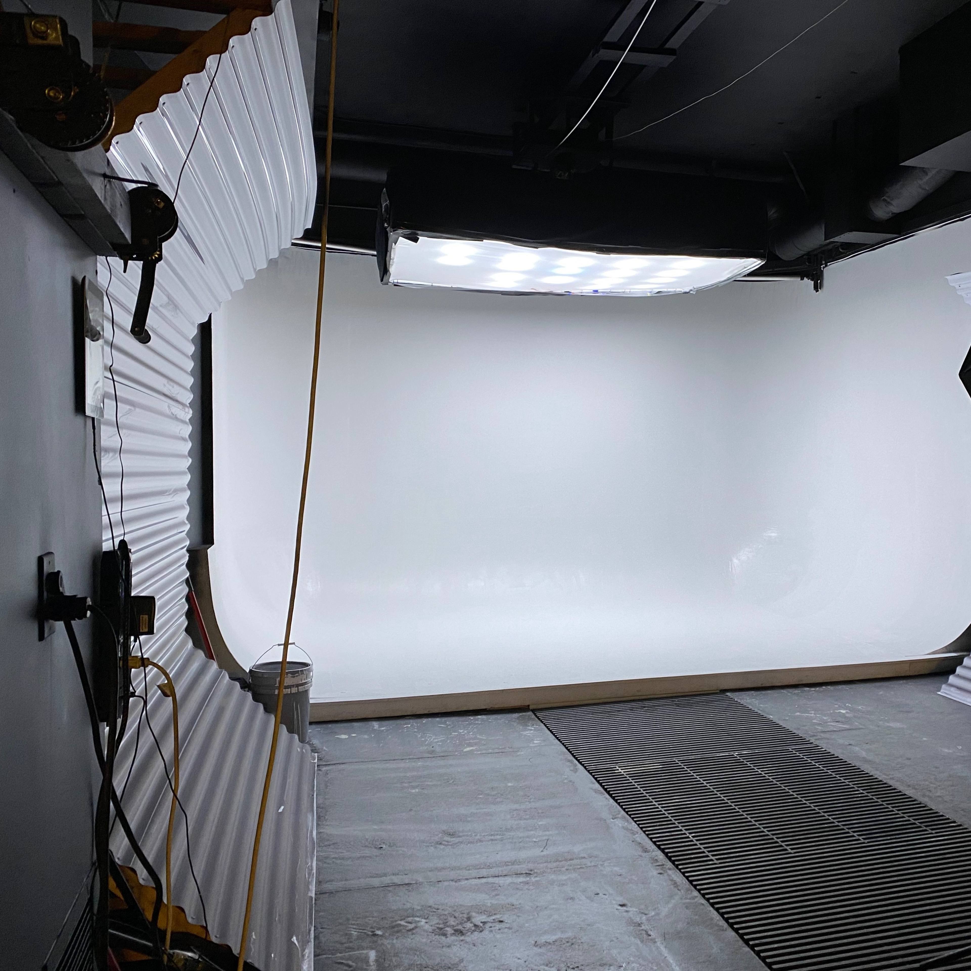 A photography studio with a seamless white backdrop and lighting equipment set up.