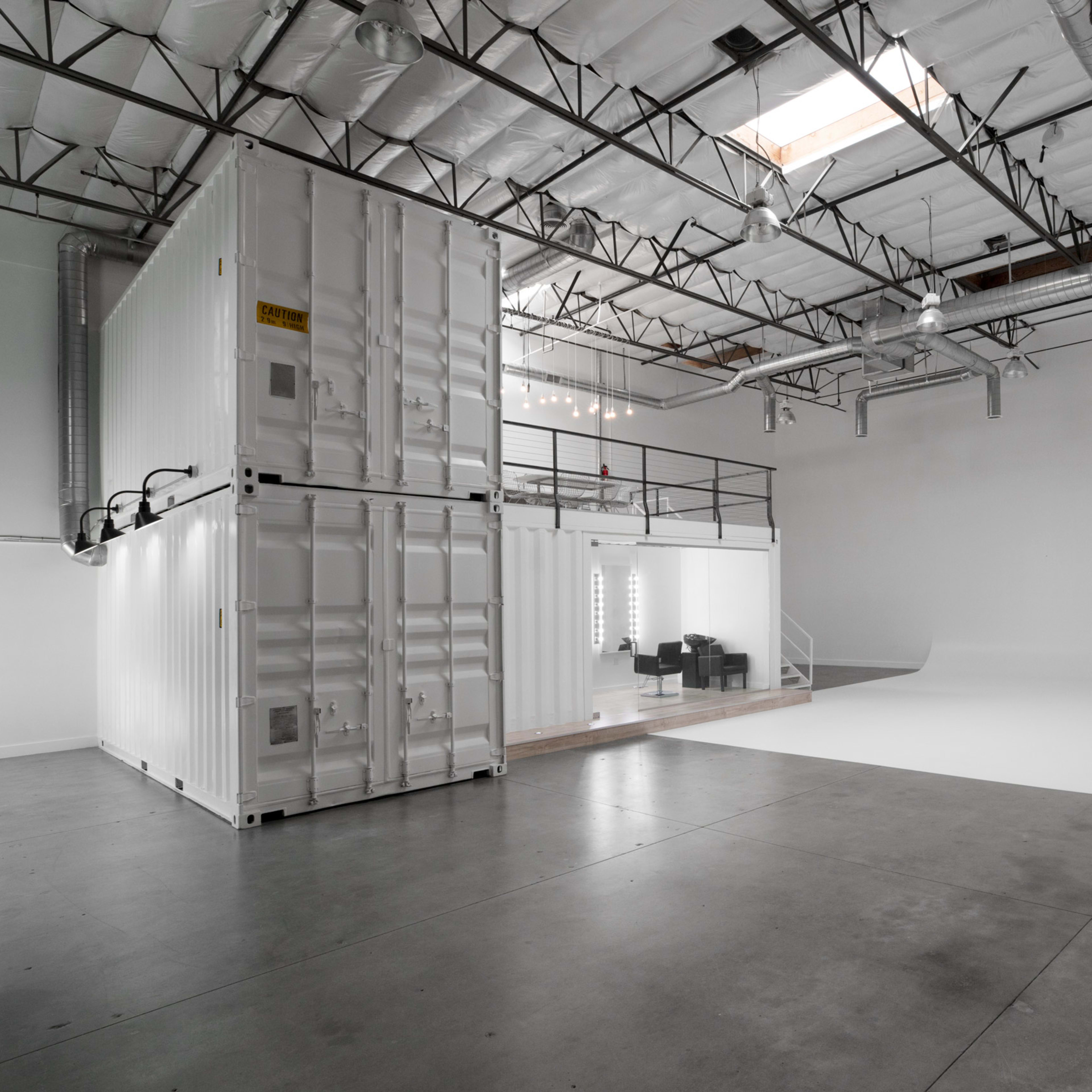 An empty studio space featuring two stacked shipping containers and a large white backdrop area.