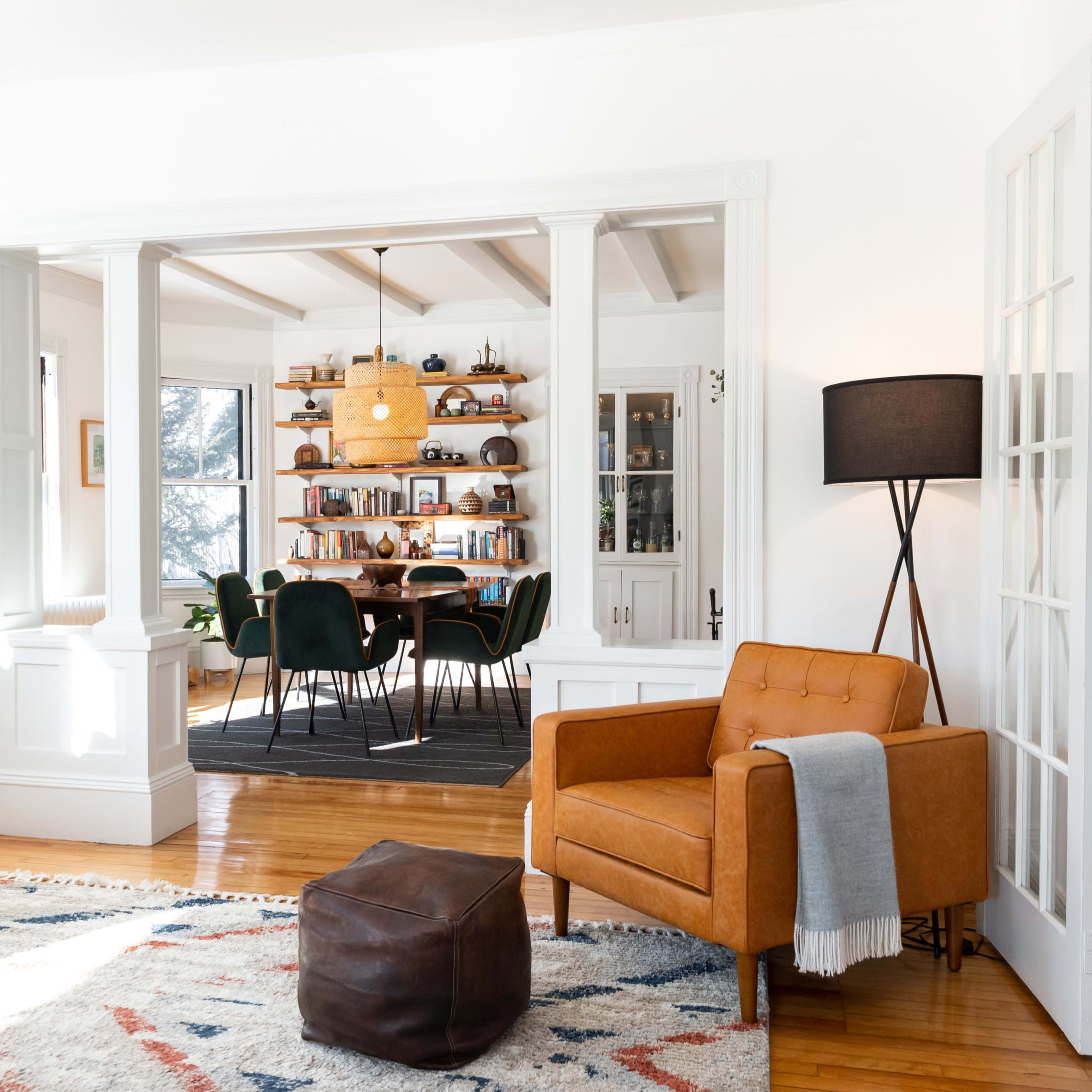 A bright living room featuring an orange armchair, a decorative rug, a television, and a view into a dining area with a wooden table and bookshelves.