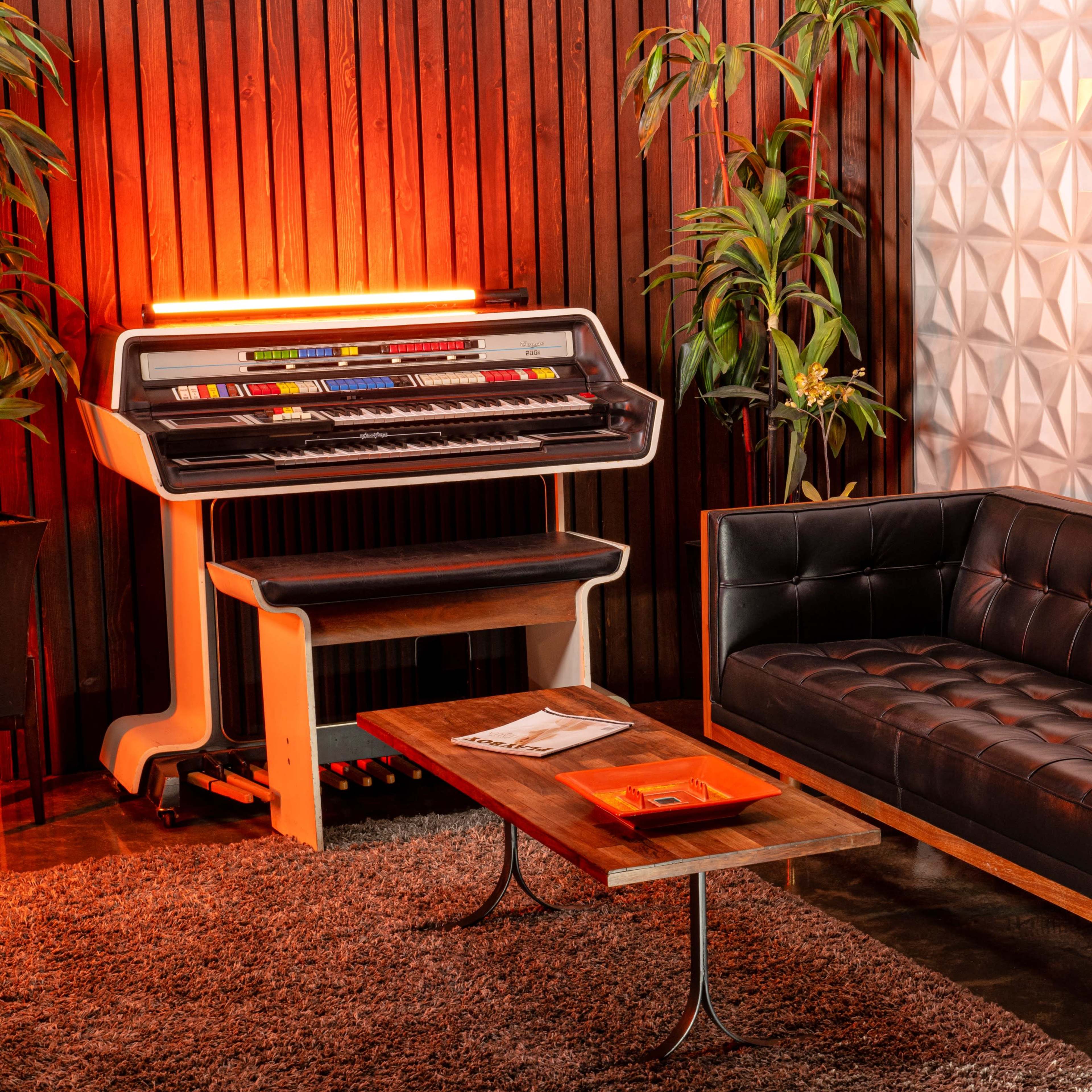 A modern living space with a black leather couch, a wooden coffee table, a vintage radio, and a colorful keyboard instrument against a backdrop of textured wall panels and indoor plants.