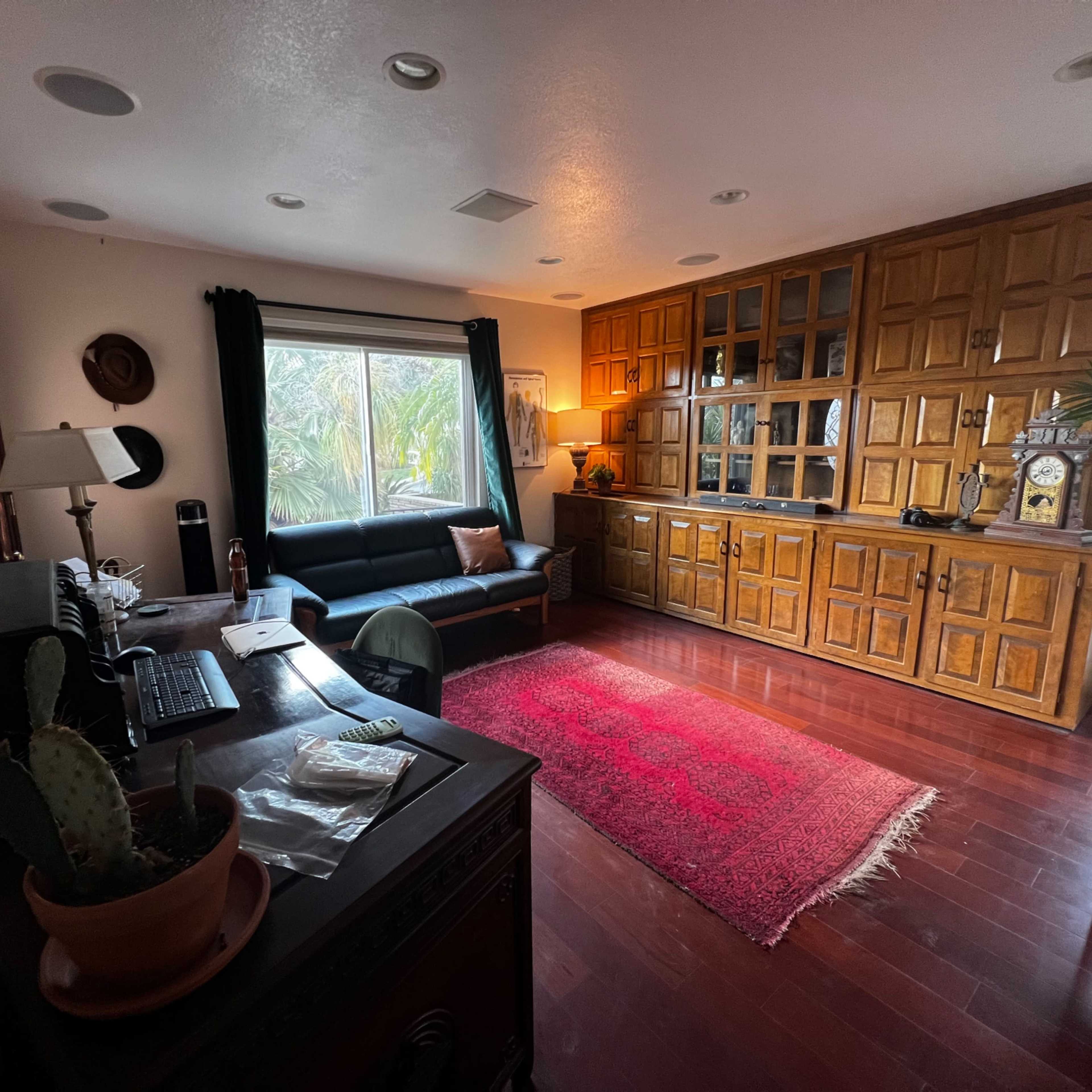 A modern living room with a dark leather sofa, a wooden cabinet, and a desk with a computer, all arranged on polished wooden flooring.
