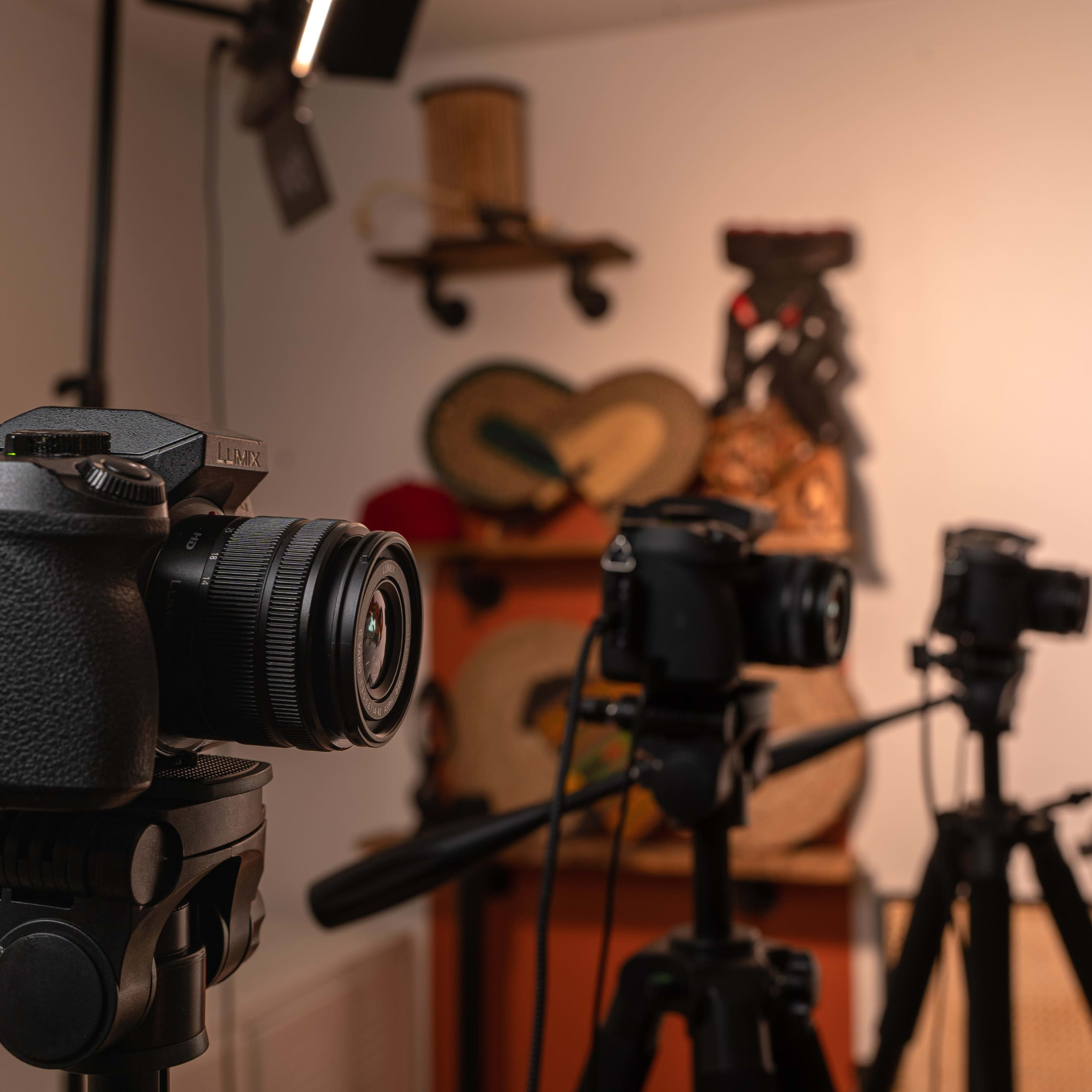 Three cameras mounted on tripods in a room adorned with decorative items on the wall.