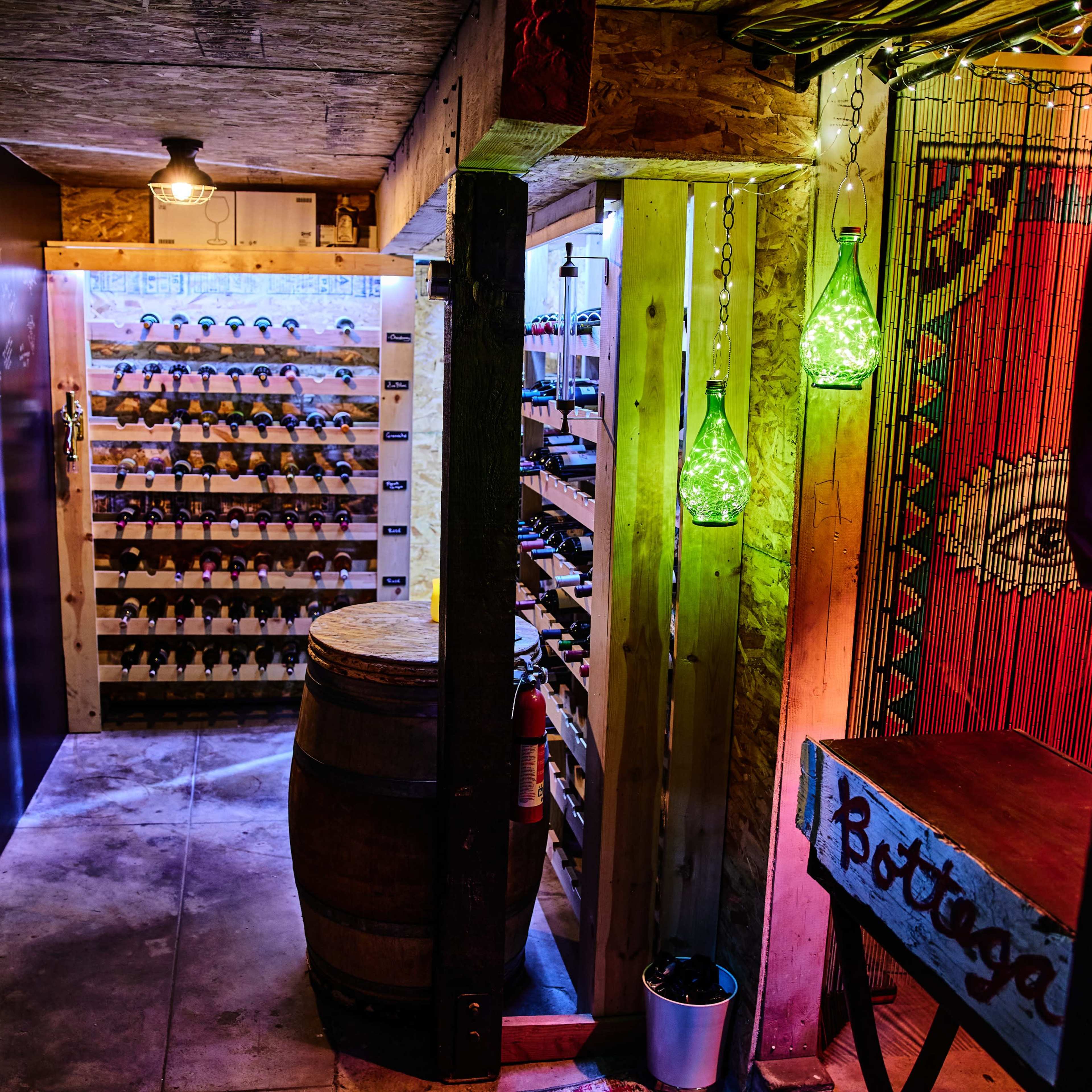 A dimly lit wine cellar with wooden shelves filled with bottles, a barrel, and decorative lighting.