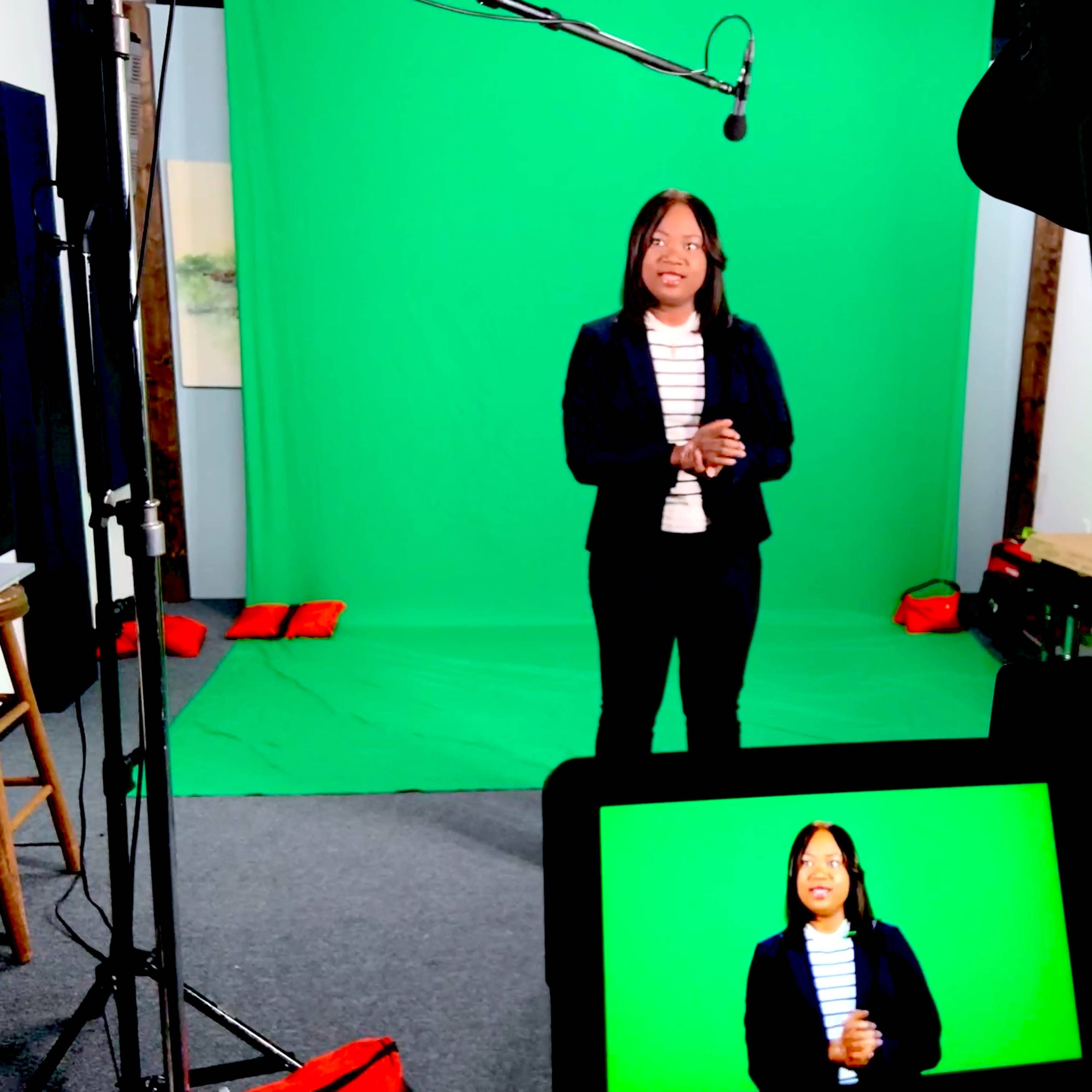 A woman stands in front of a green screen set, with cameras and equipment positioned to capture her presentation.