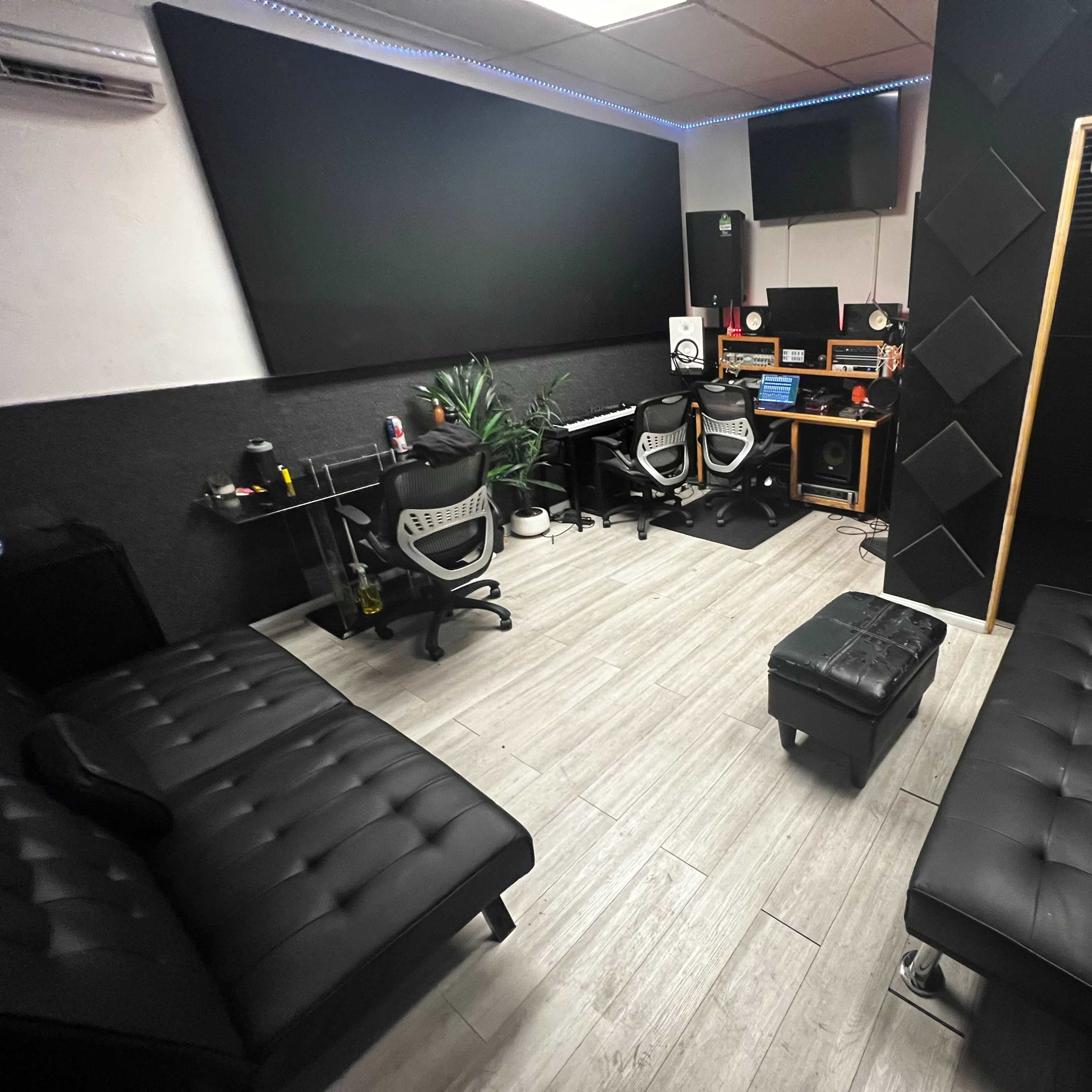A recording studio with two black couches, a mixing desk, and sound equipment arranged in a sleek, minimalist layout.