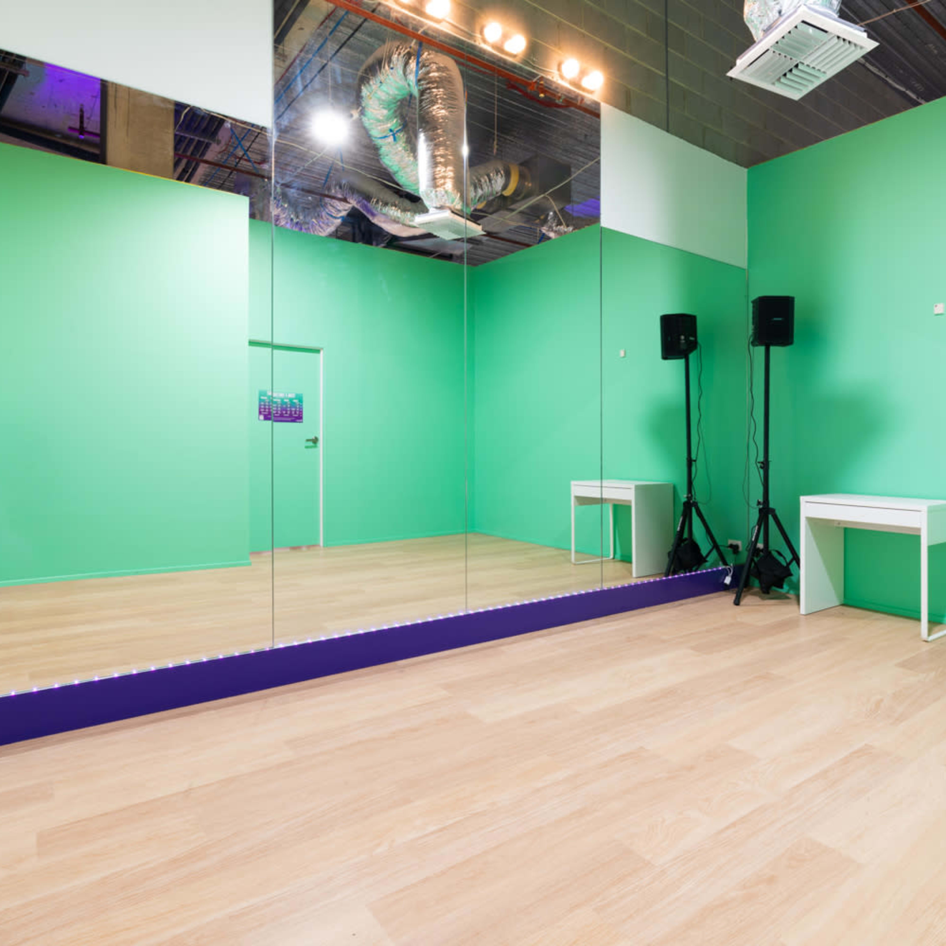 A bright green empty room with a large mirror on one wall, a small white table, and audio equipment in the corners.
