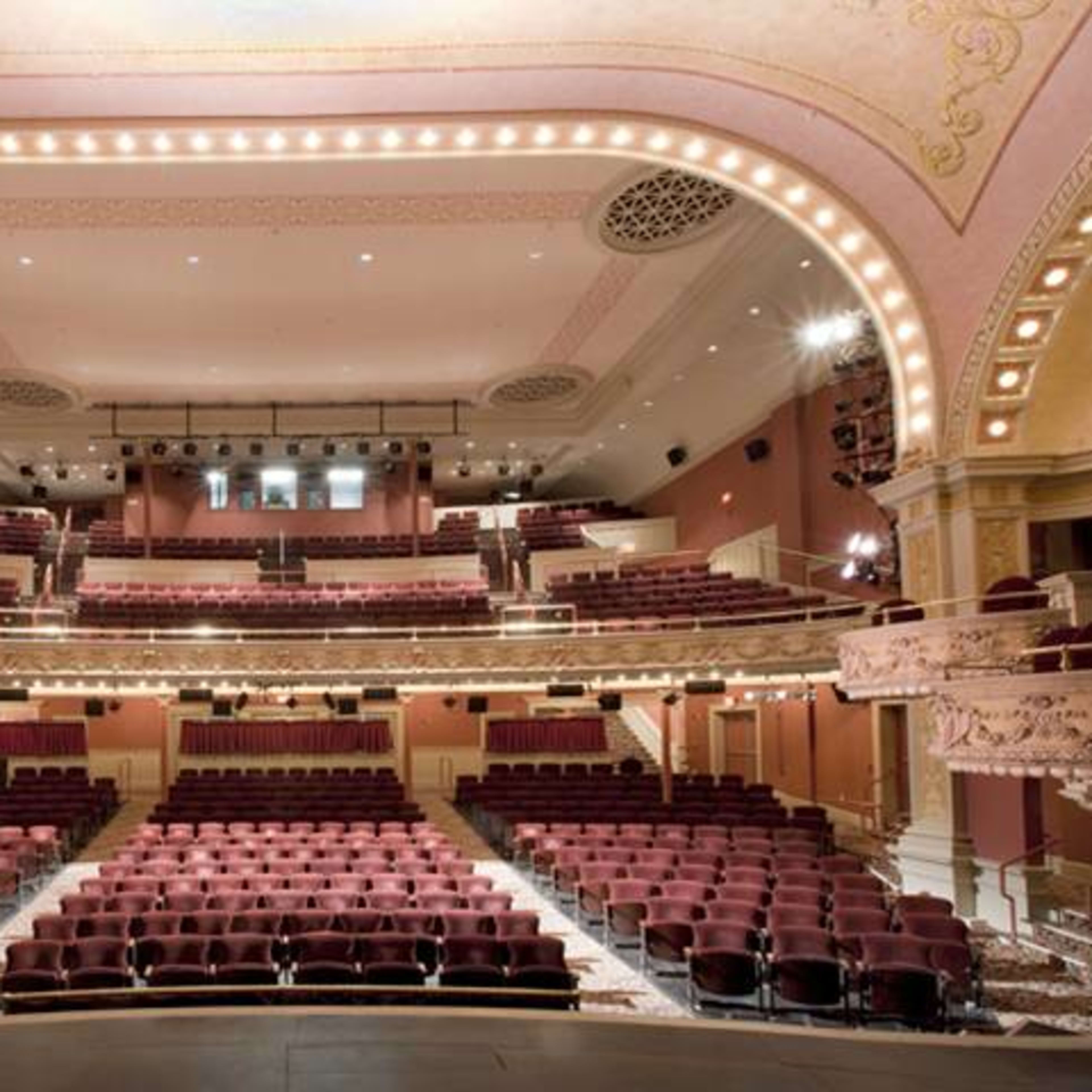 The interior of a theater featuring a grand stage, multiple levels of seating, and ornate architectural details.