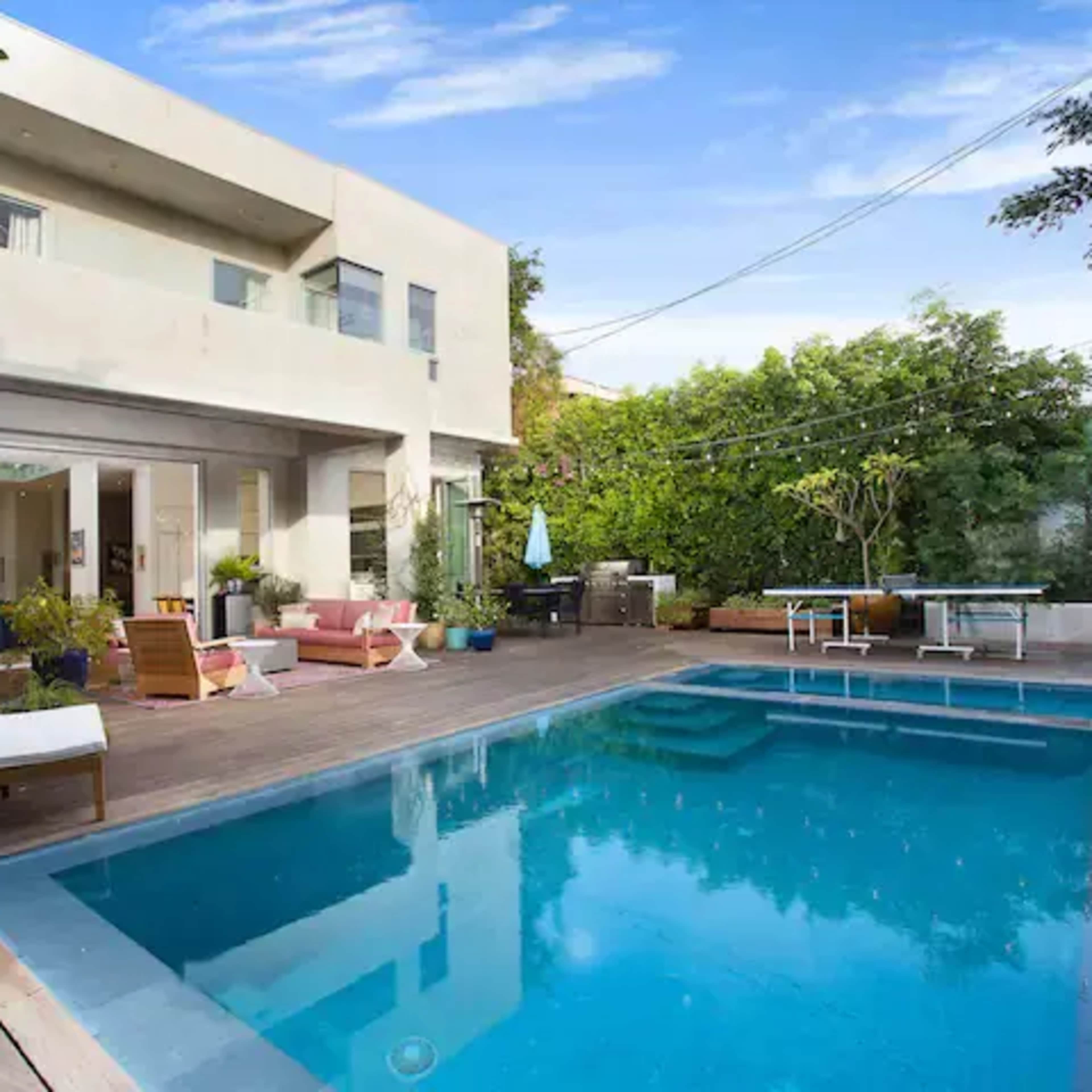 A modern house with a swimming pool is surrounded by lush greenery and outdoor seating areas.
