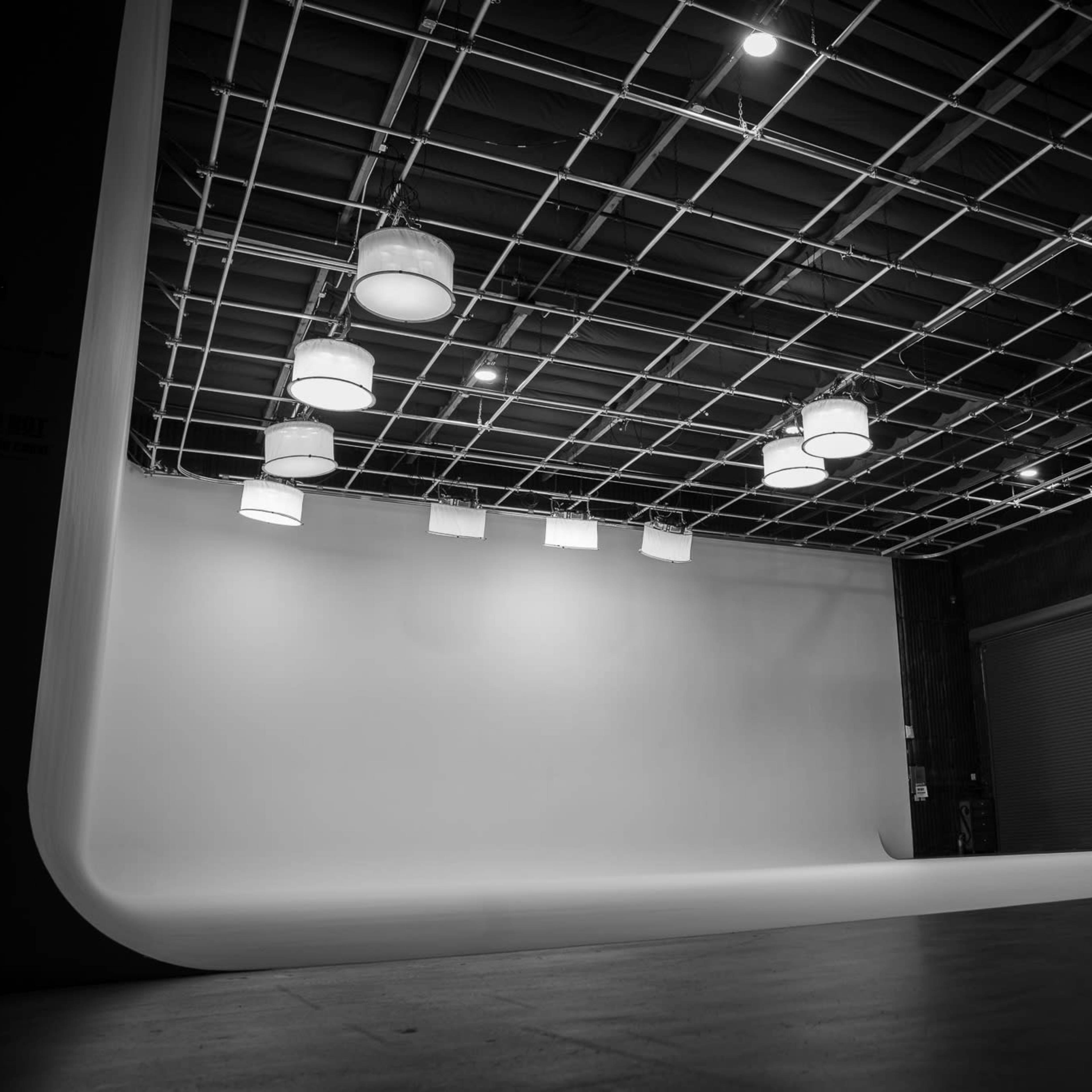An empty photography studio with a white backdrop and overhead lighting fixtures.