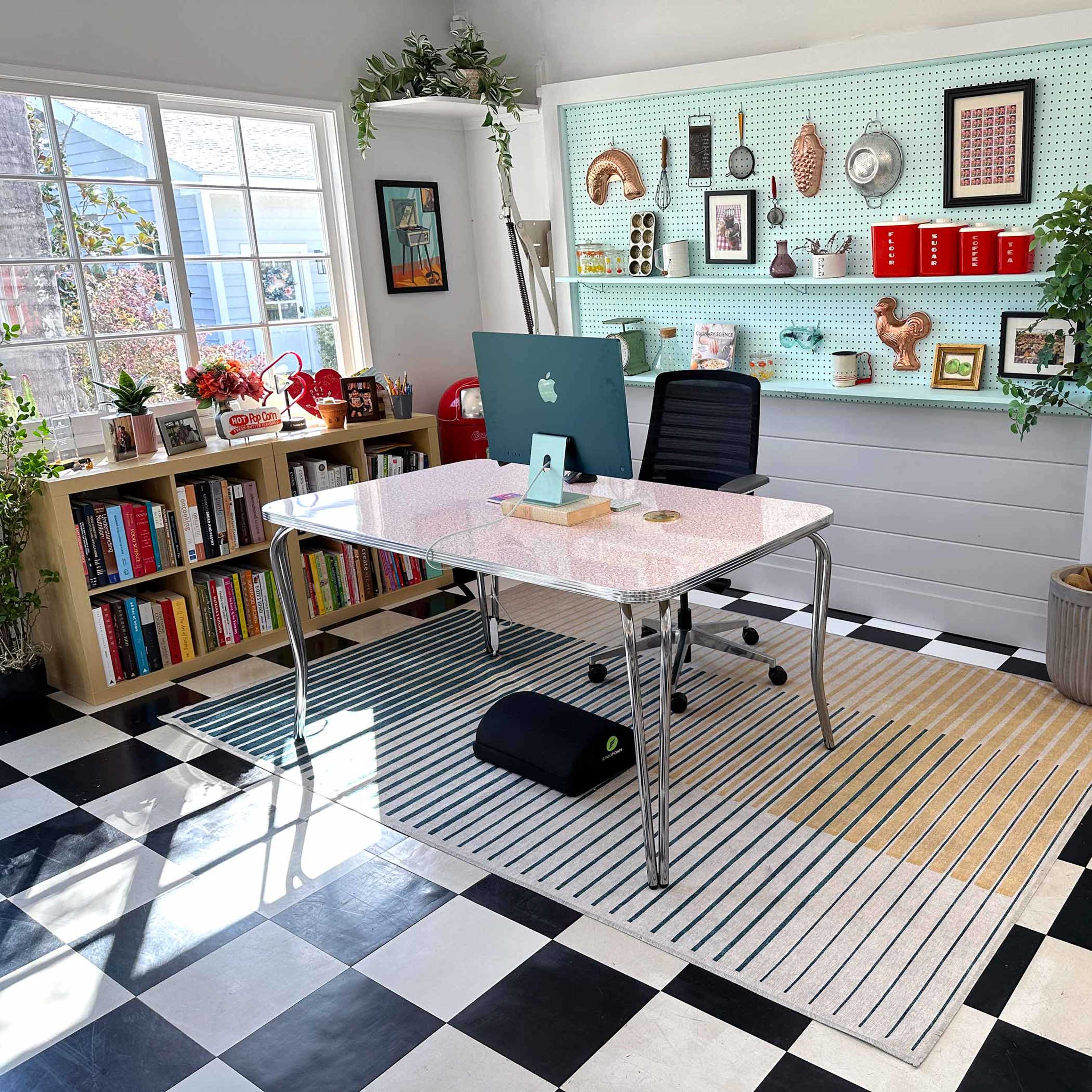 A modern office features a sleek glass desk with a computer, shelving with various decorative items, and a patterned black and white floor.