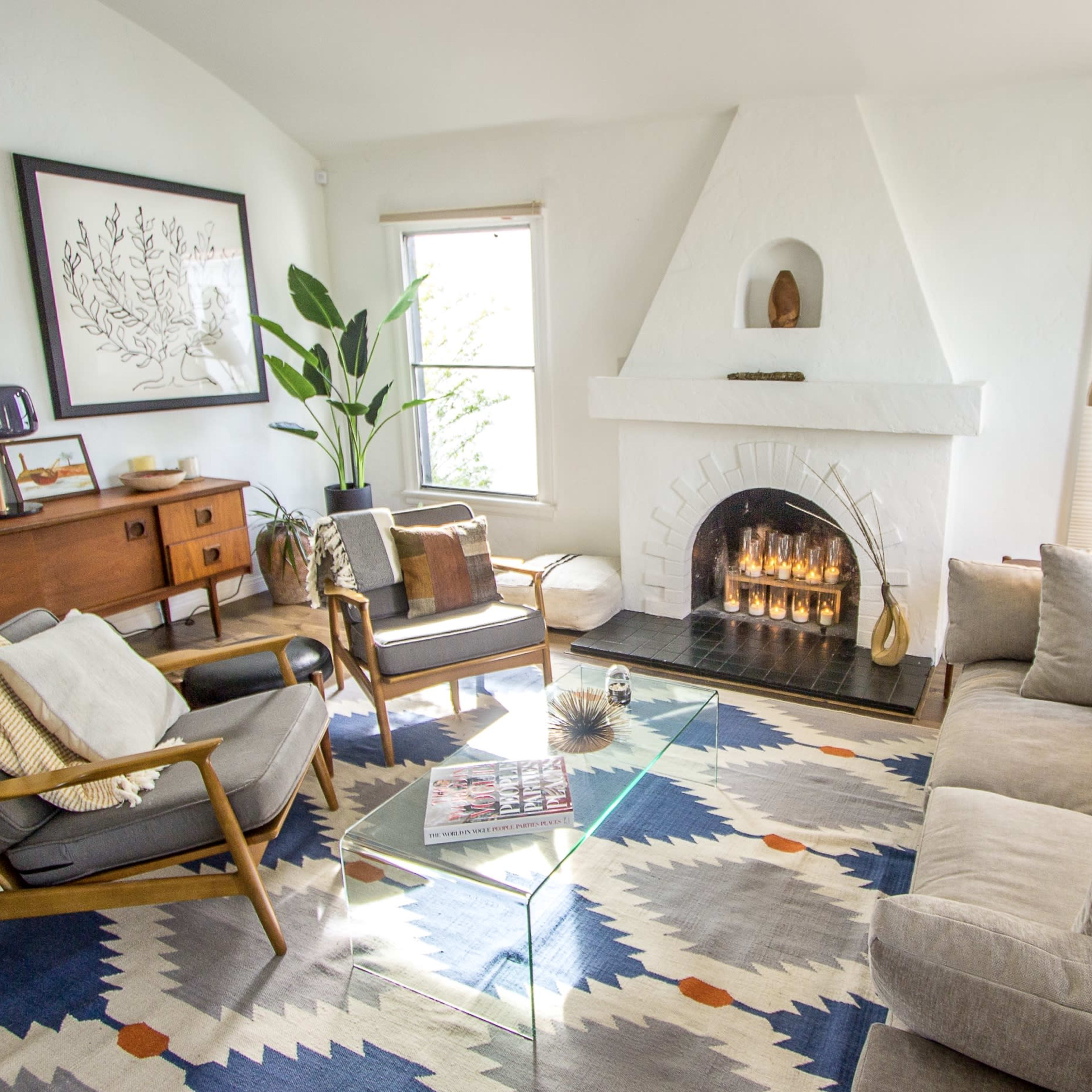 A modern living room featuring a fireplace, a large sofa, stylish chairs, and a geometric area rug.
