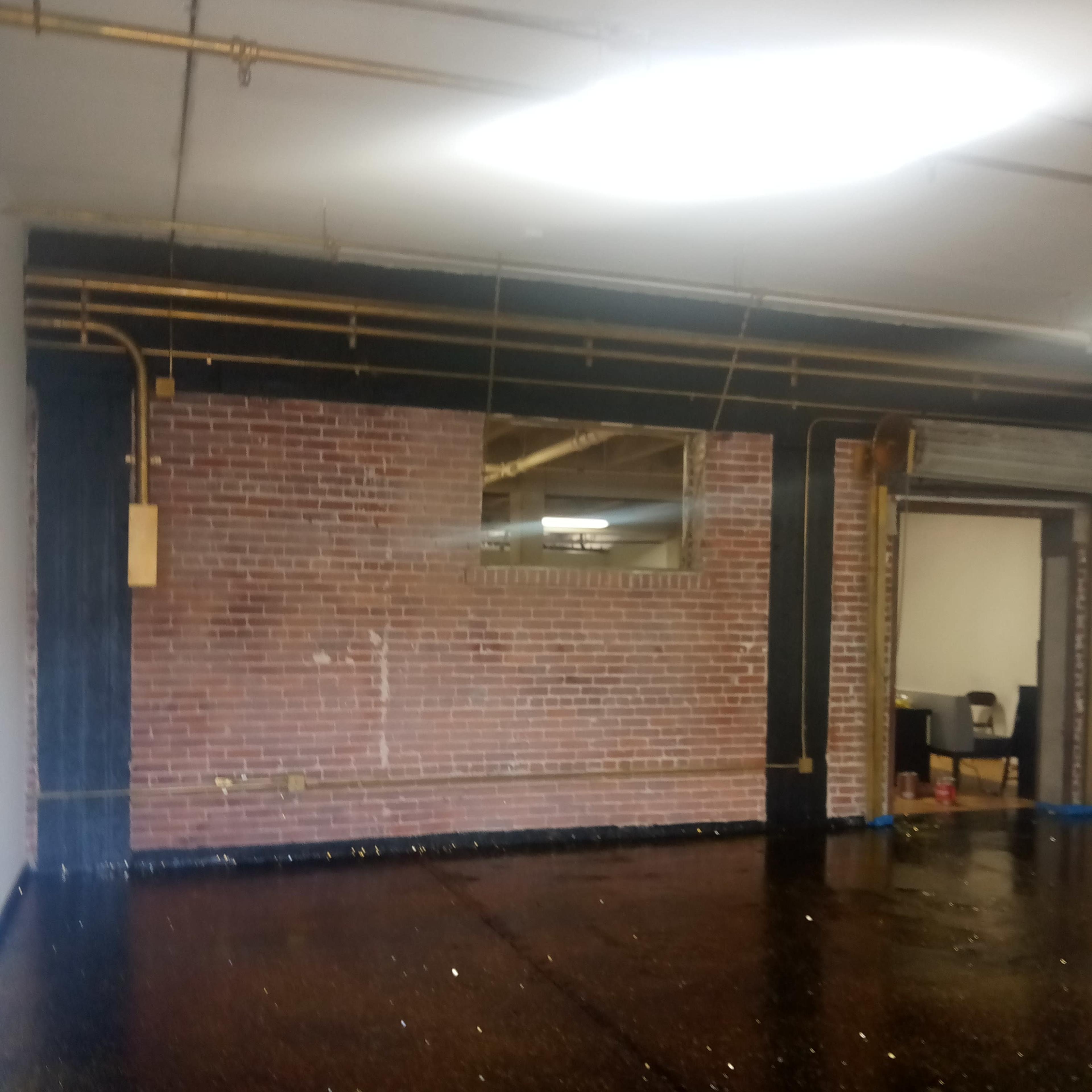 A spacious industrial-style room with a brick wall, a mirror, and a glossy black floor speckled with gold glitter.