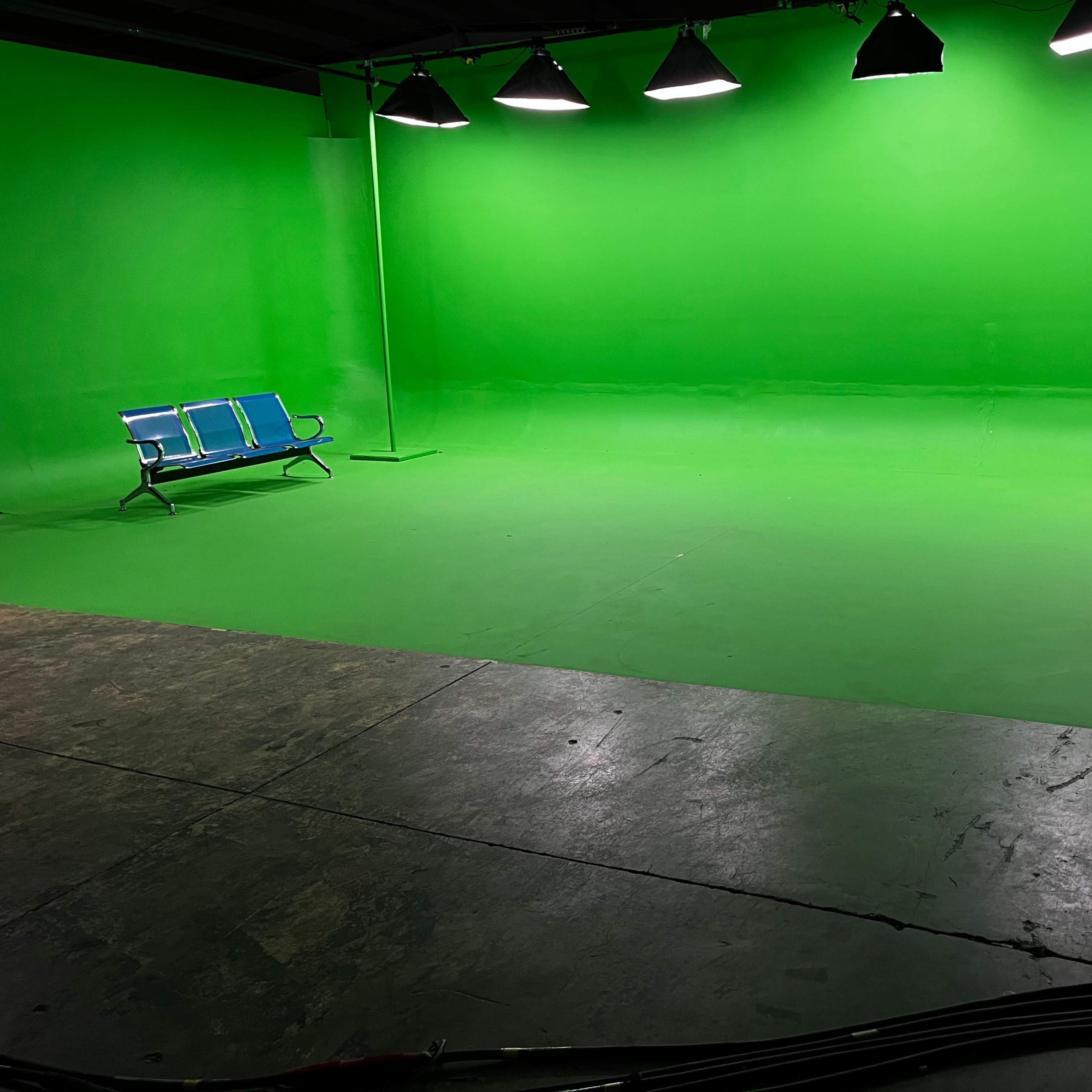 A green screen studio featuring two blue benches and a small table on a concrete floor.
