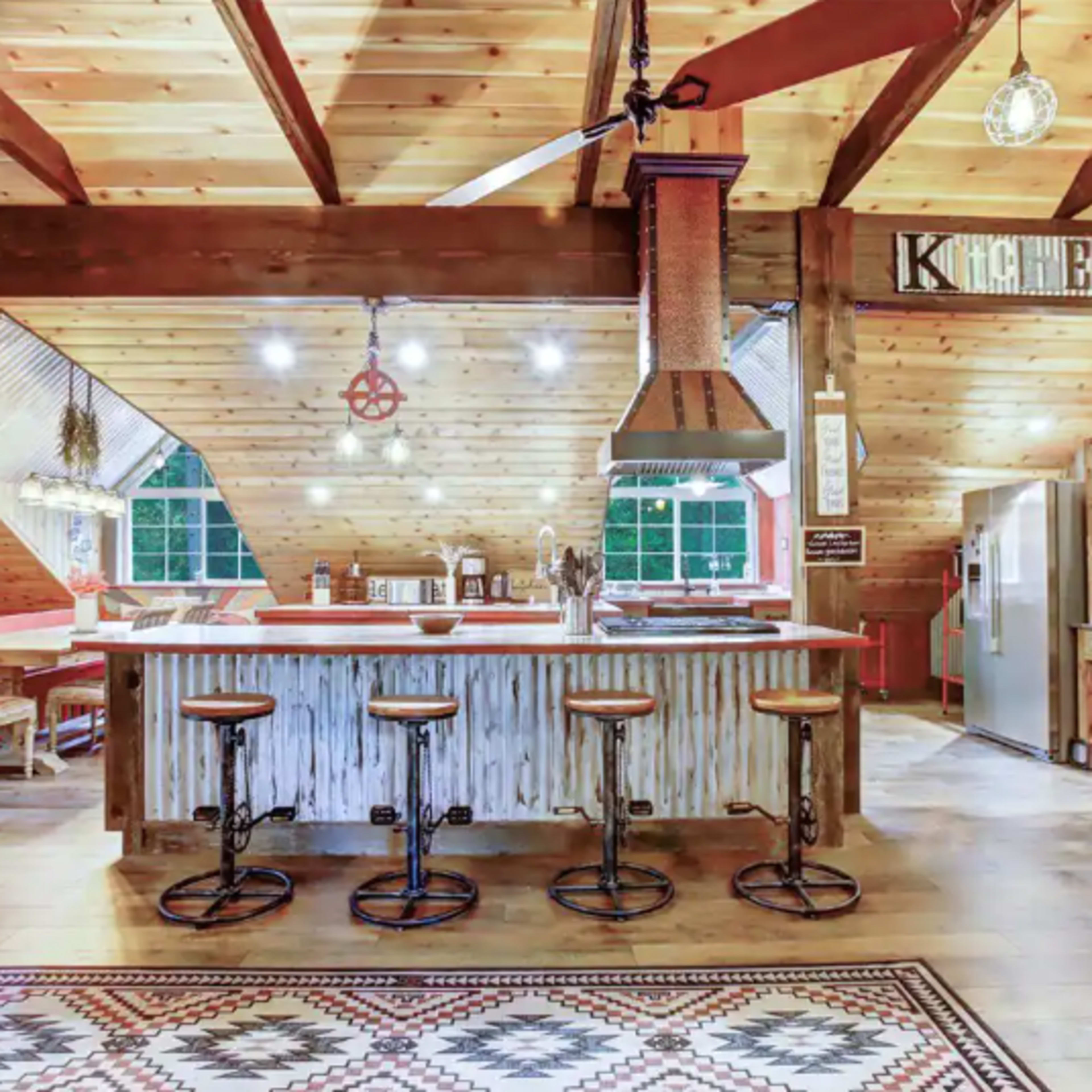 A spacious, rustic kitchen with wooden beams, a large island with metal accents, and three bar stools.