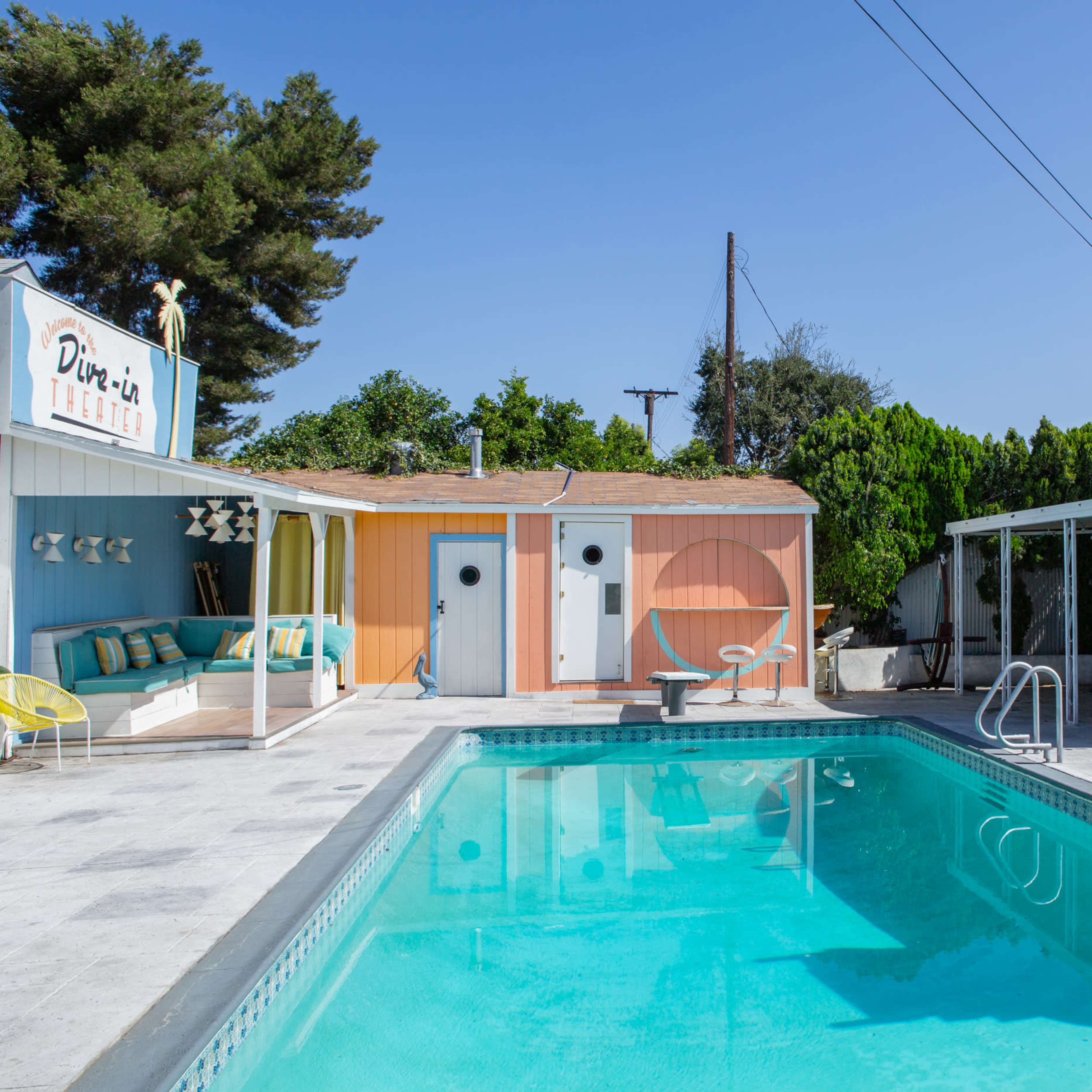 A vibrant pool area surrounded by colorful cabins and a diving board in a sunny outdoor setting.