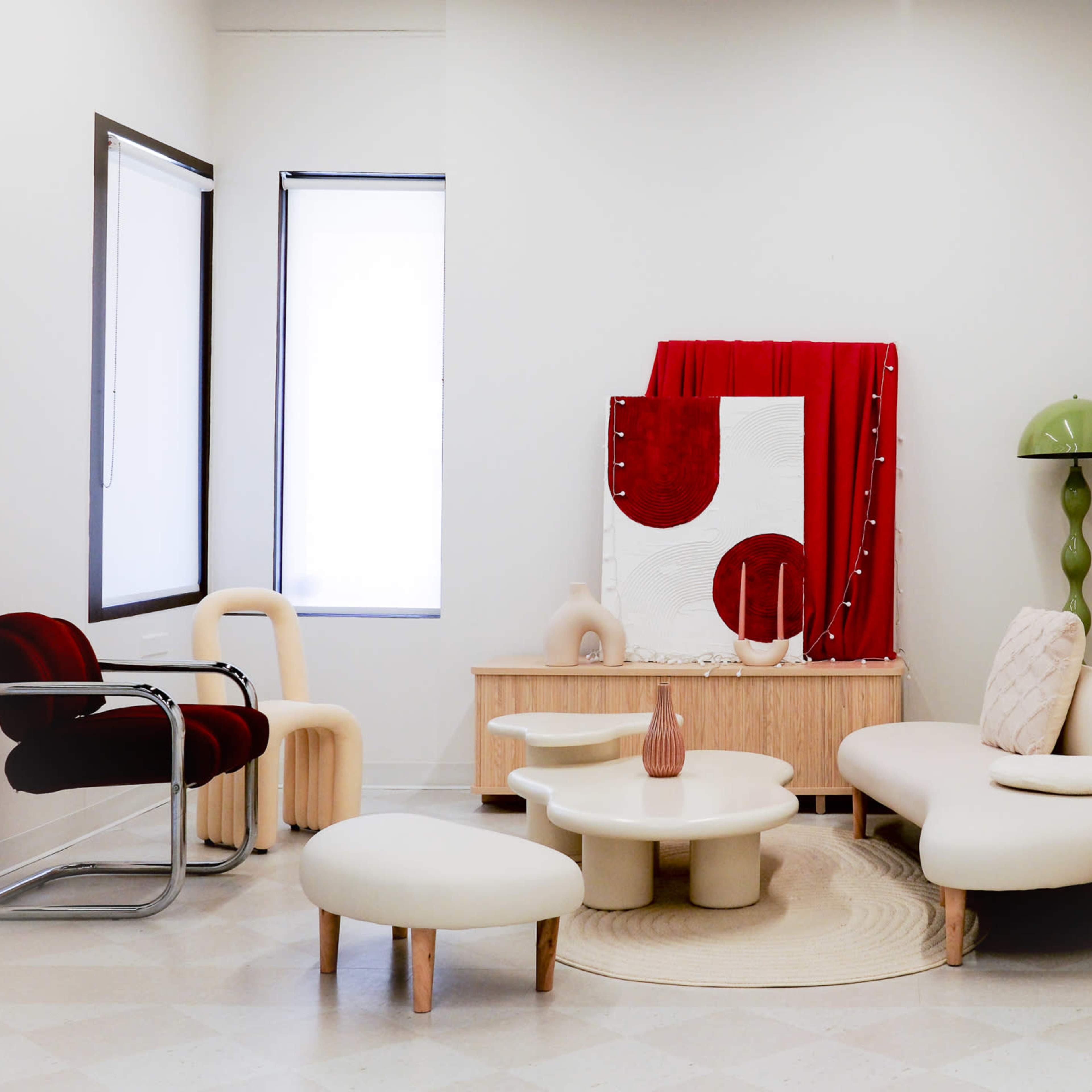 The room features modern furniture, including a red chair, a white sofa, a round coffee table, and a cabinet, with decorative elements like a tall green lamp and a large red backdrop.