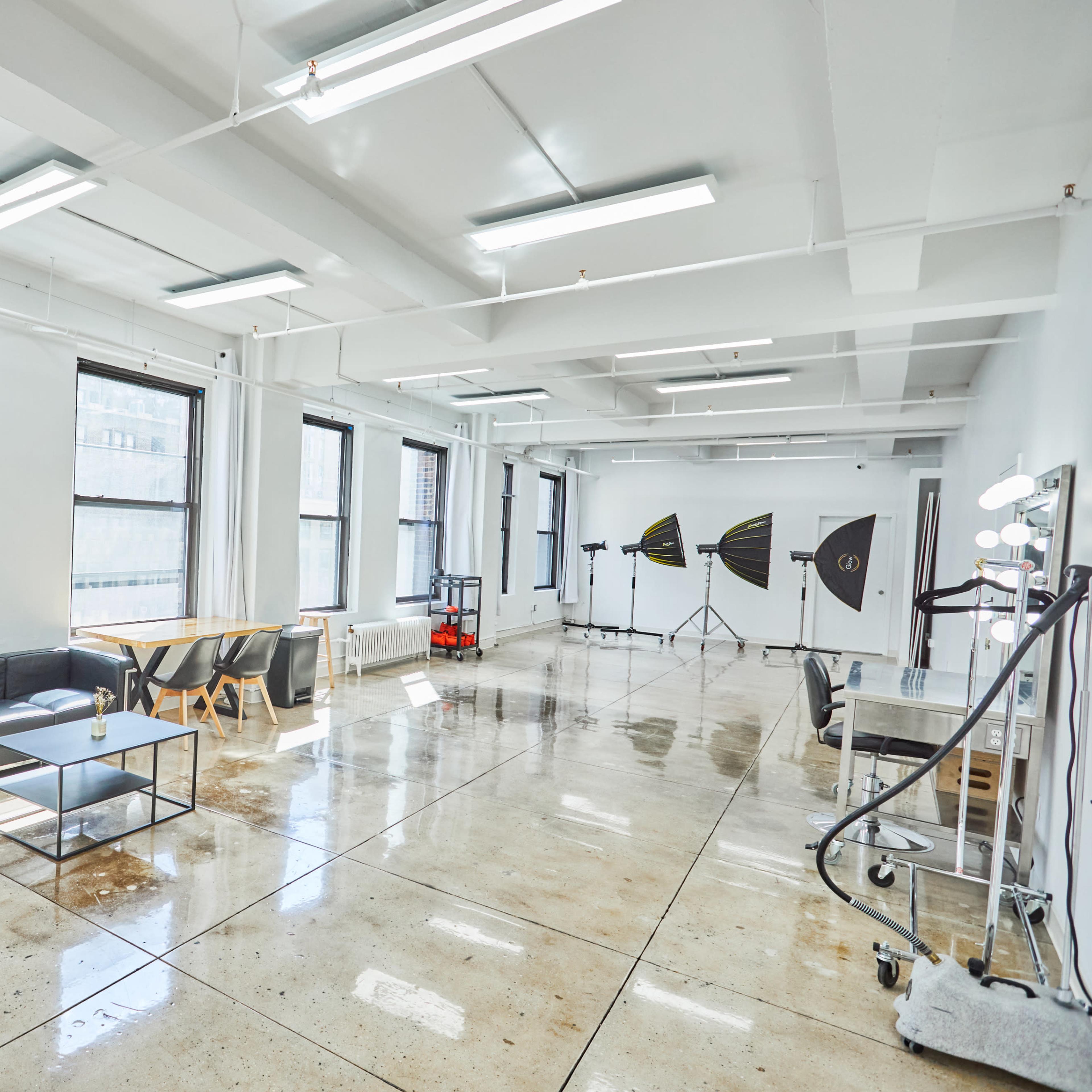 A spacious room with large windows, modern furniture, and a setup for photography with backdrop stands and lighting equipment.