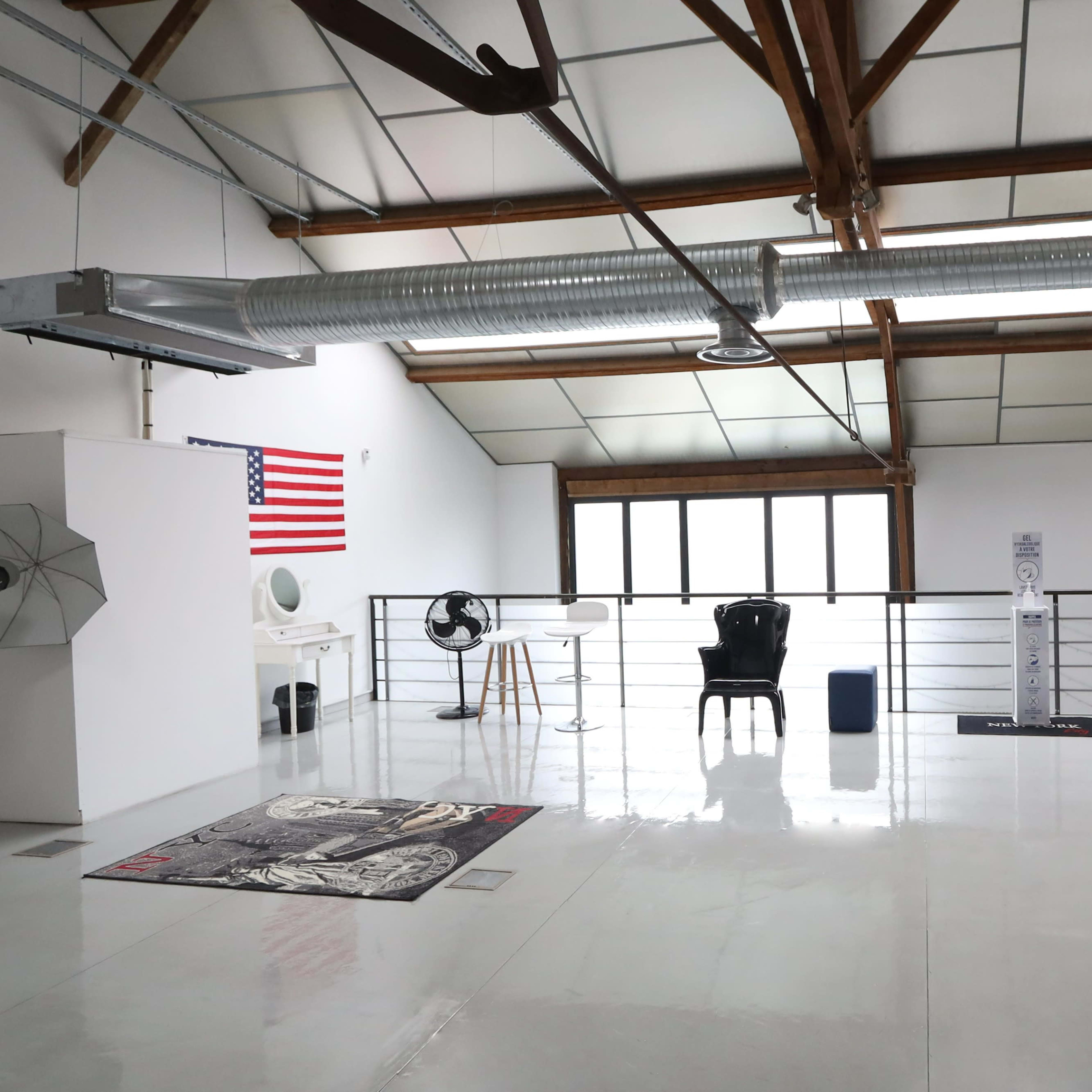 A spacious, airy room with high ceilings, featuring an American flag, various furnishings, and large windows.
