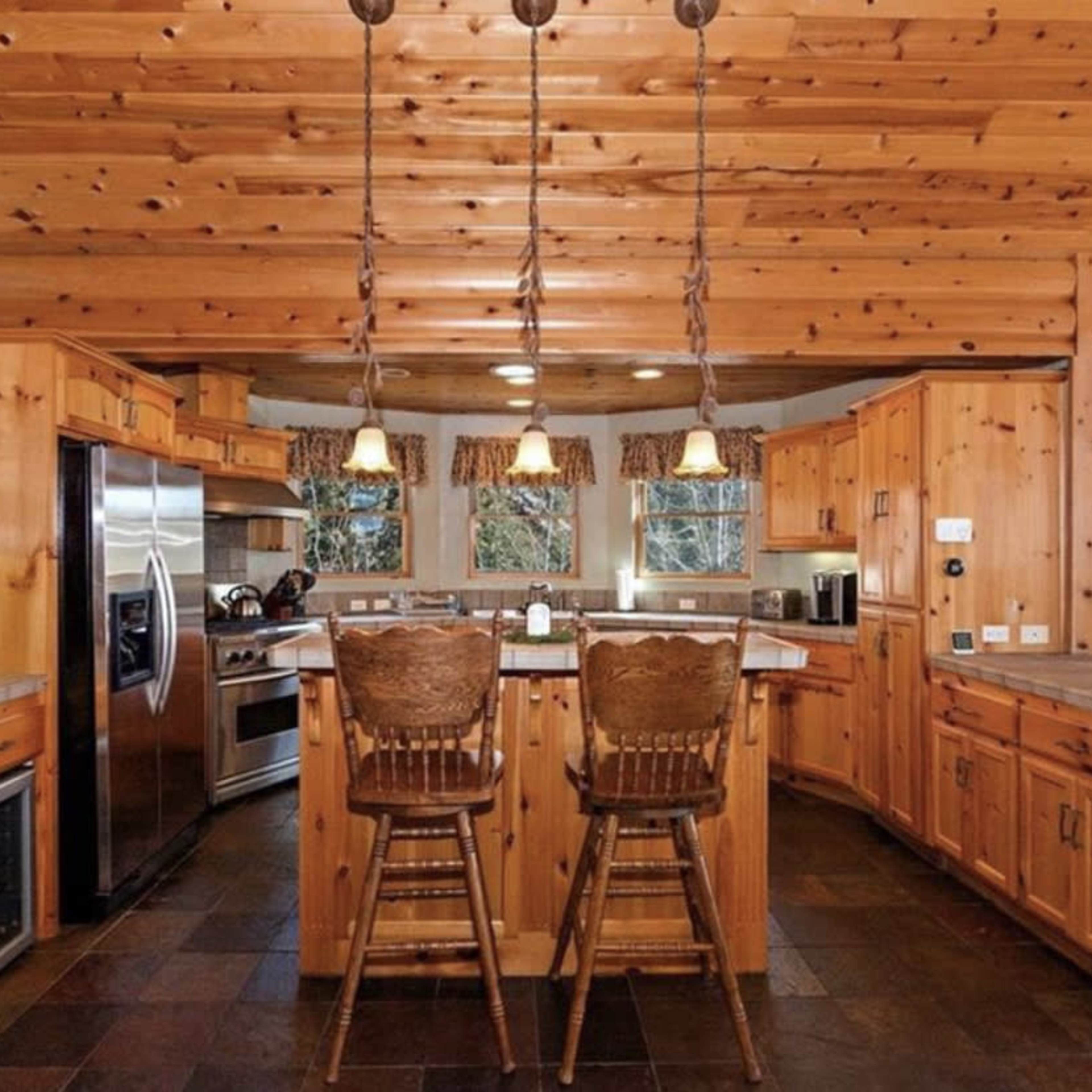 A kitchen with wooden cabinetry, a stone floor, and bar stools at a counter with pendant lighting overhead.