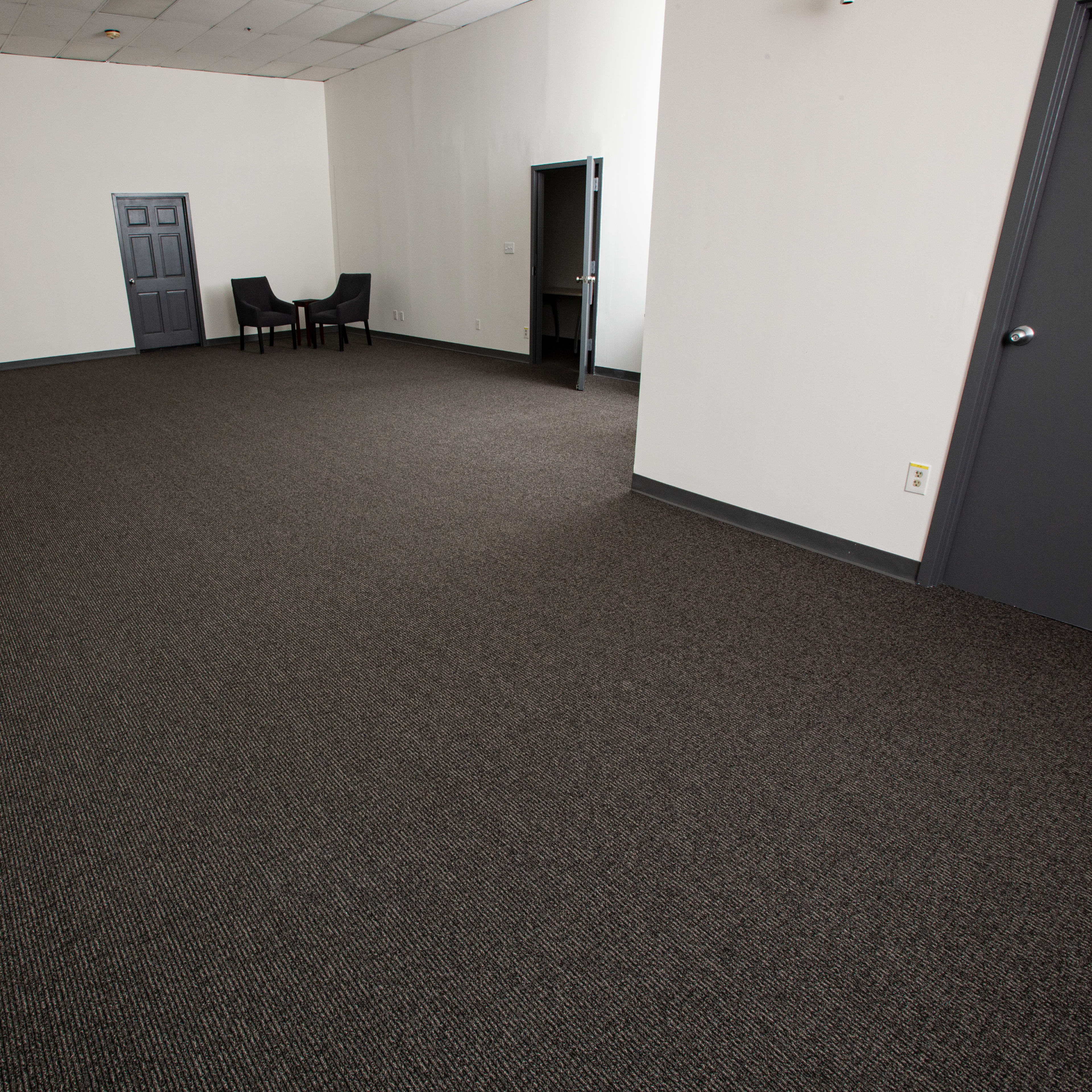 An empty room with gray walls, a dark carpeted floor, and two chairs positioned against one wall.