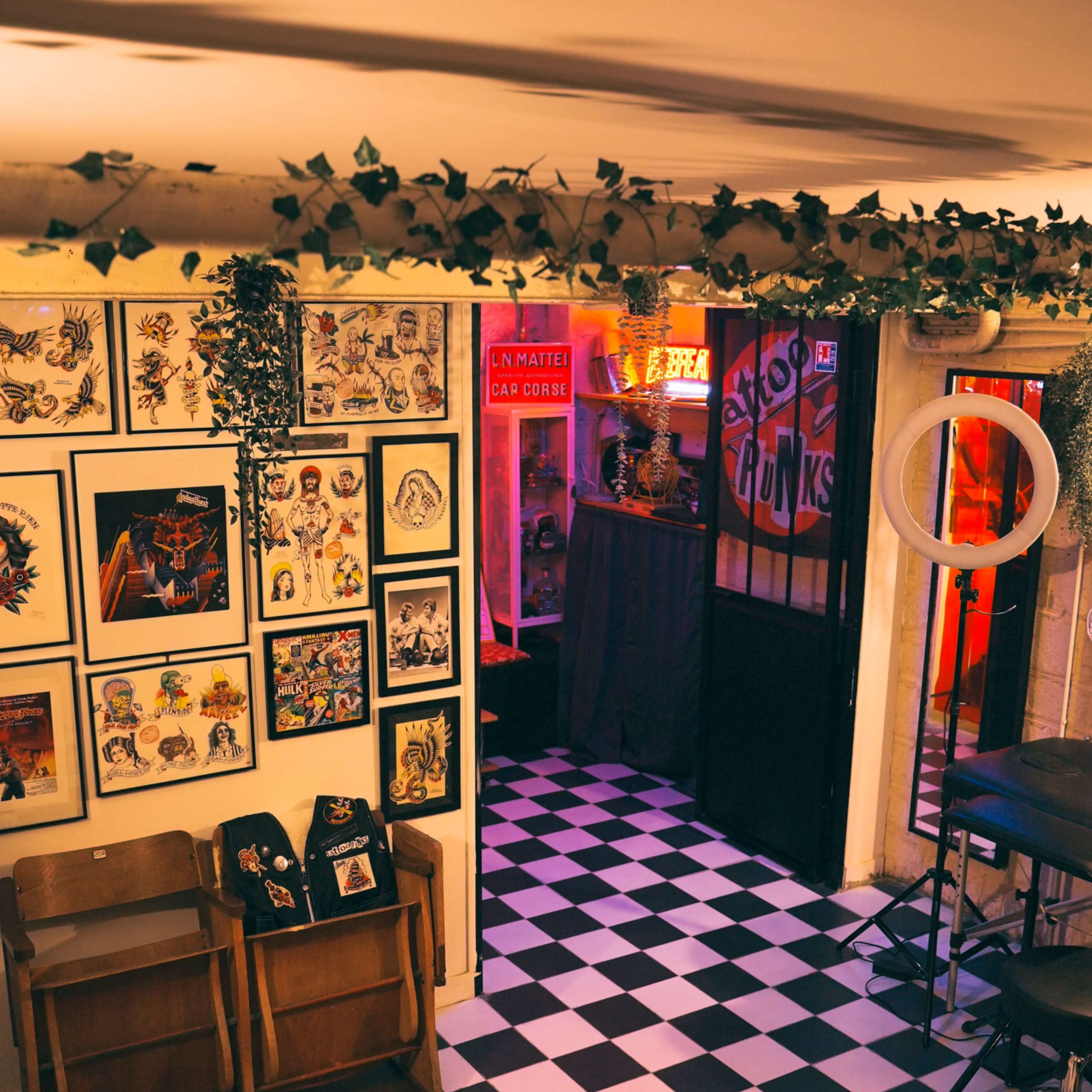 The interior of a cafe featuring a black-and-white checkered floor, framed artwork on the walls, and a dimly lit doorway leading to a separate area.