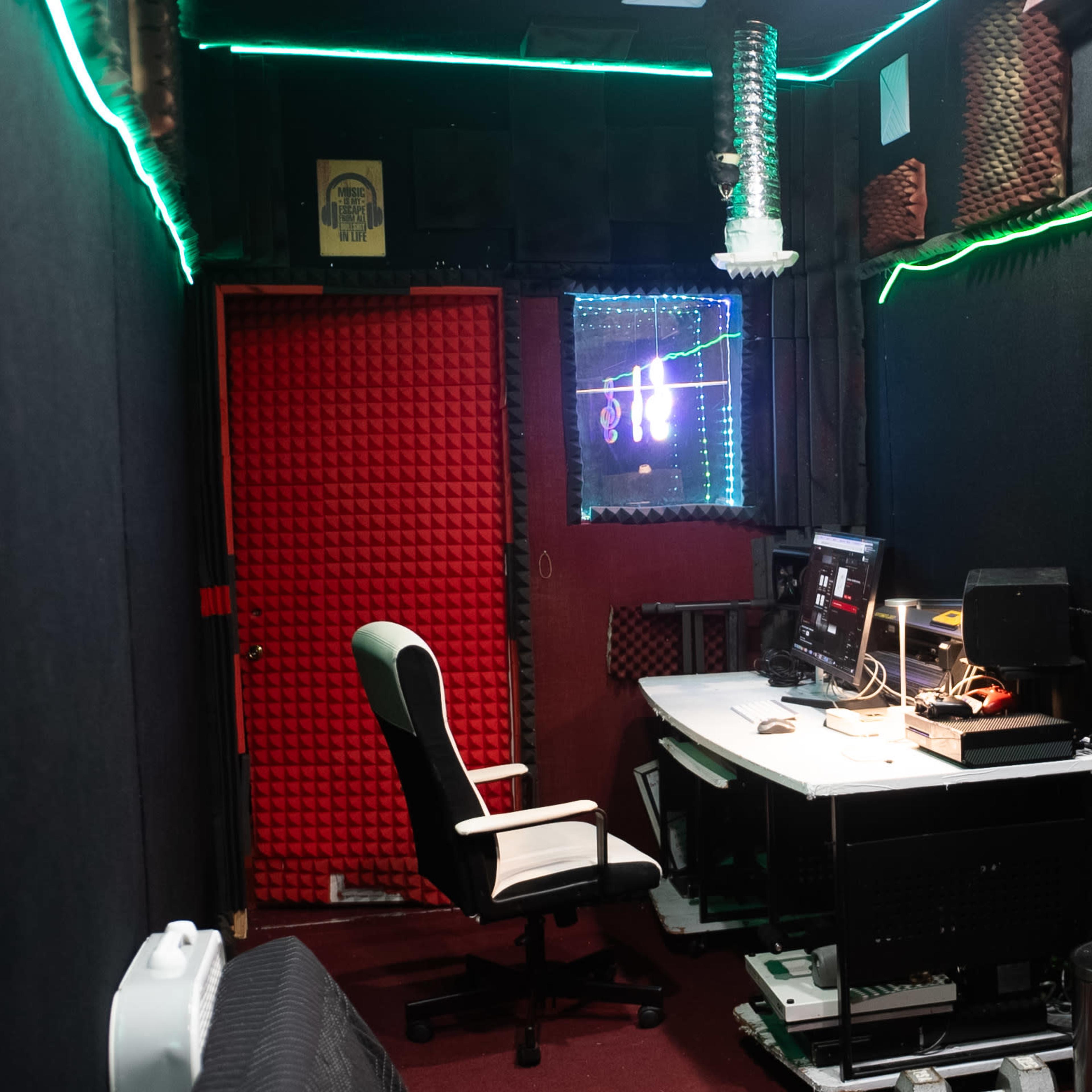 A recording studio with soundproof walls, a desk featuring audio equipment, and a red door.