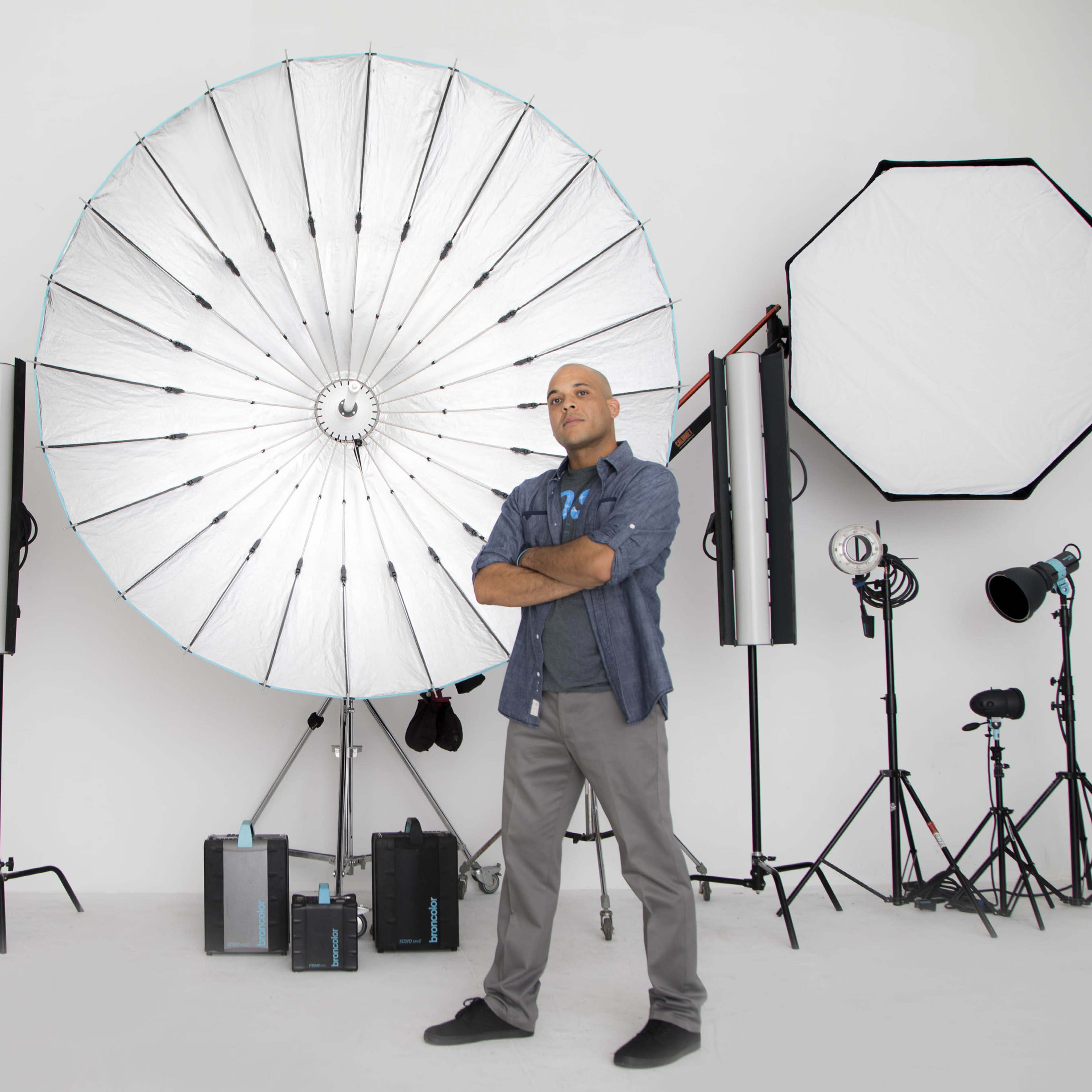A man stands confidently in front of various photography lighting equipment arranged in a studio setting.