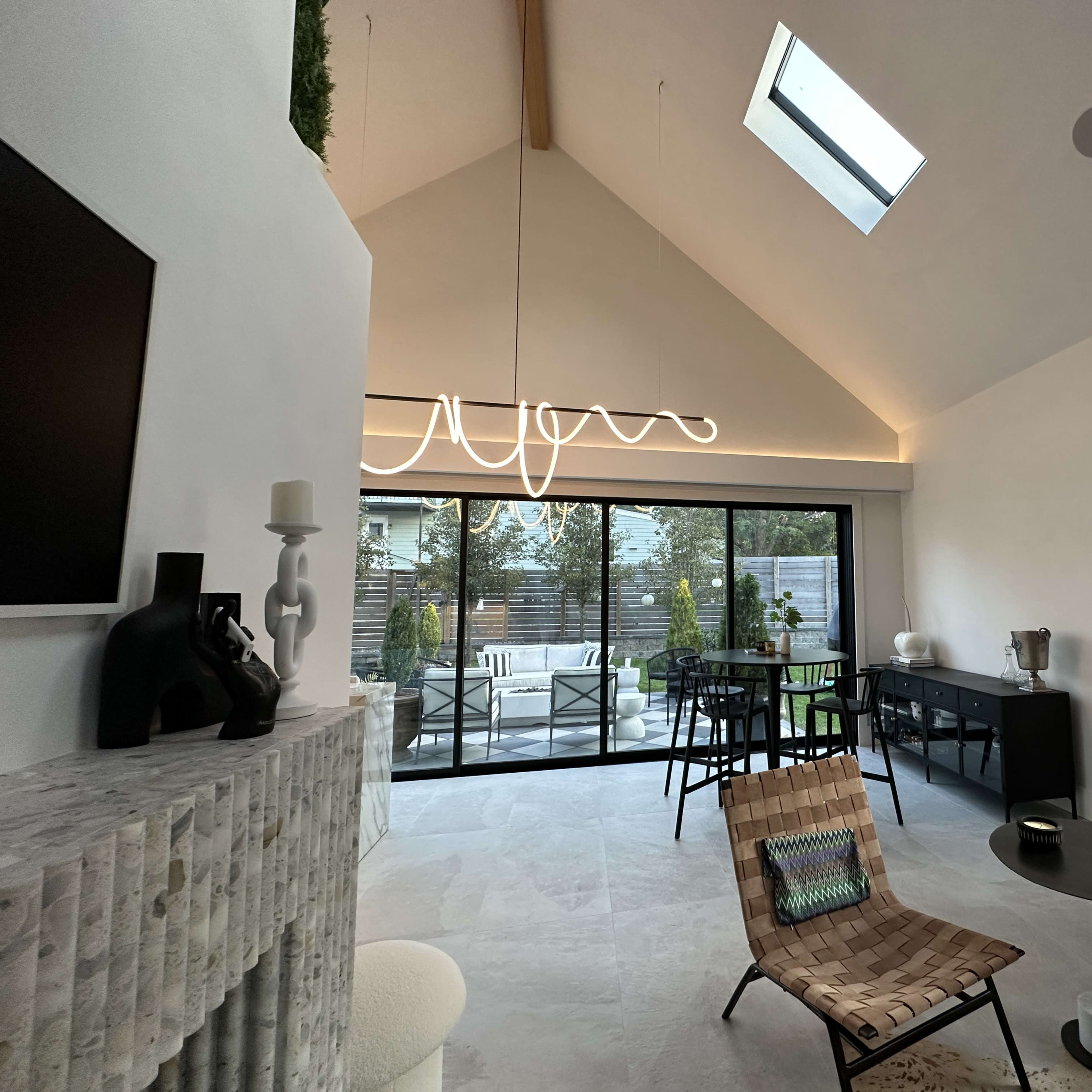A modern living space featuring a minimalistic interior design with a large glass door leading to a patio, a stylish light fixture, and a blend of contemporary furniture.