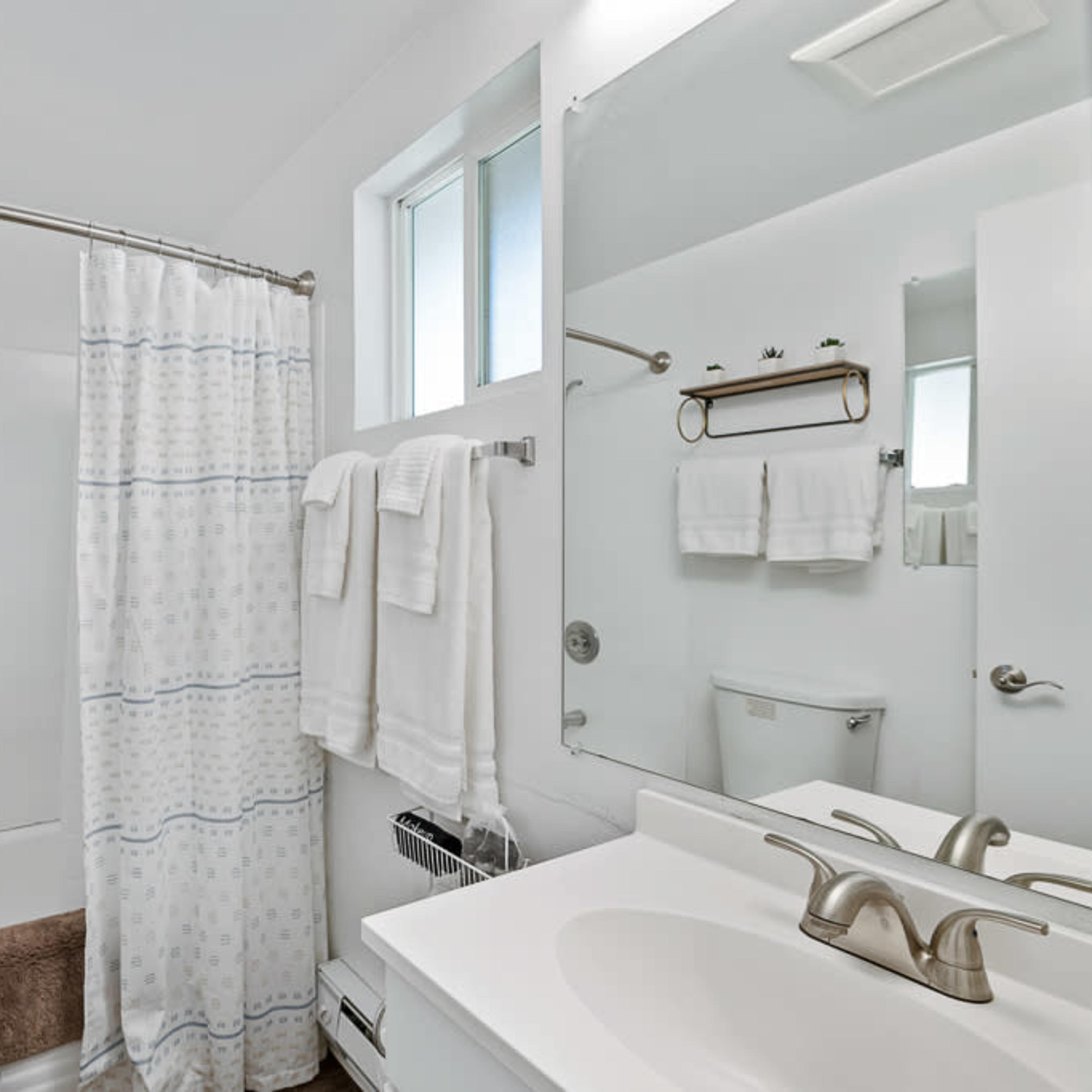 A bathroom featuring a bathtub with a shower curtain, a sink with a mirror, and neatly arranged towels on a rack.
