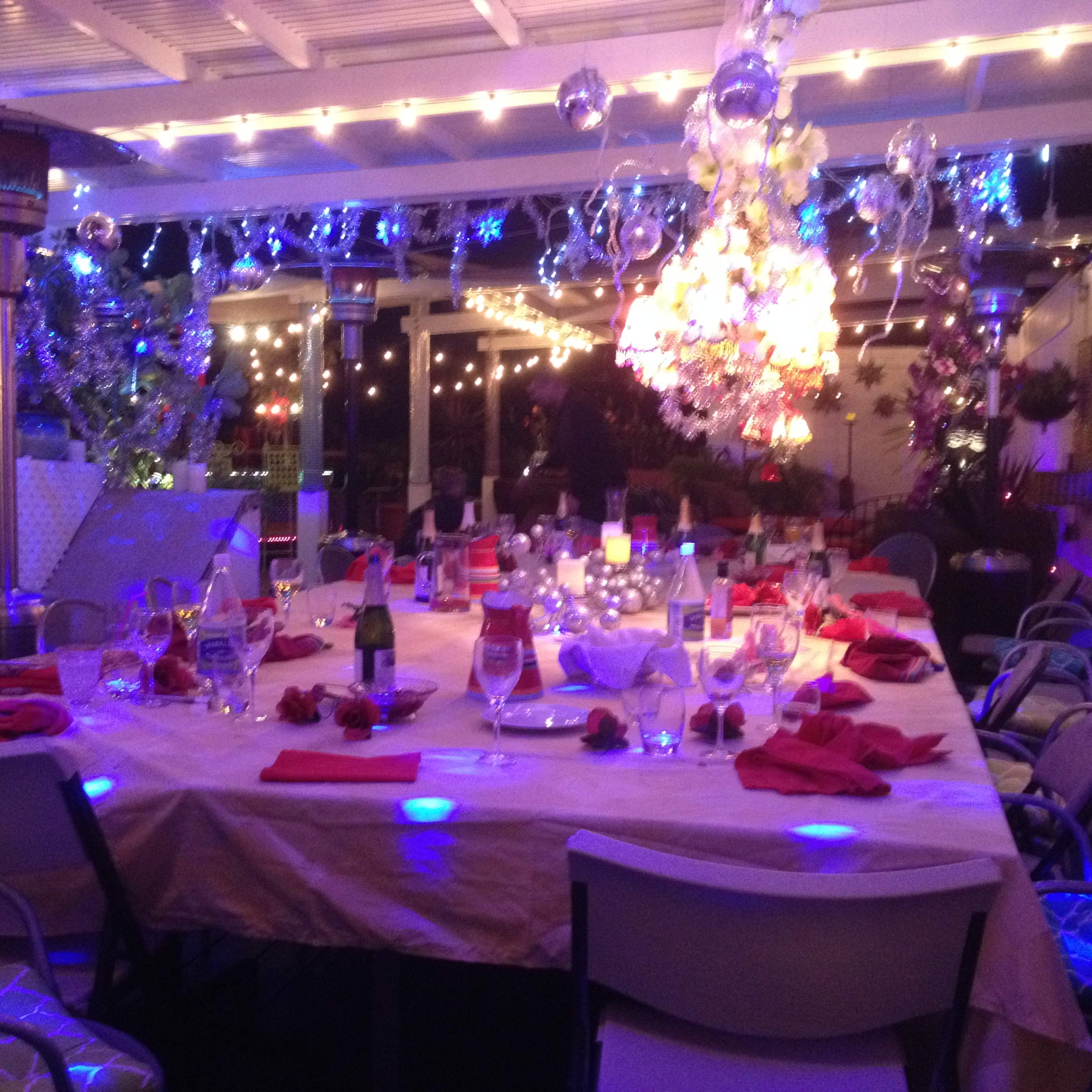 A dining setup under a pergola, adorned with string lights and decorative elements, ready for a festive gathering.
