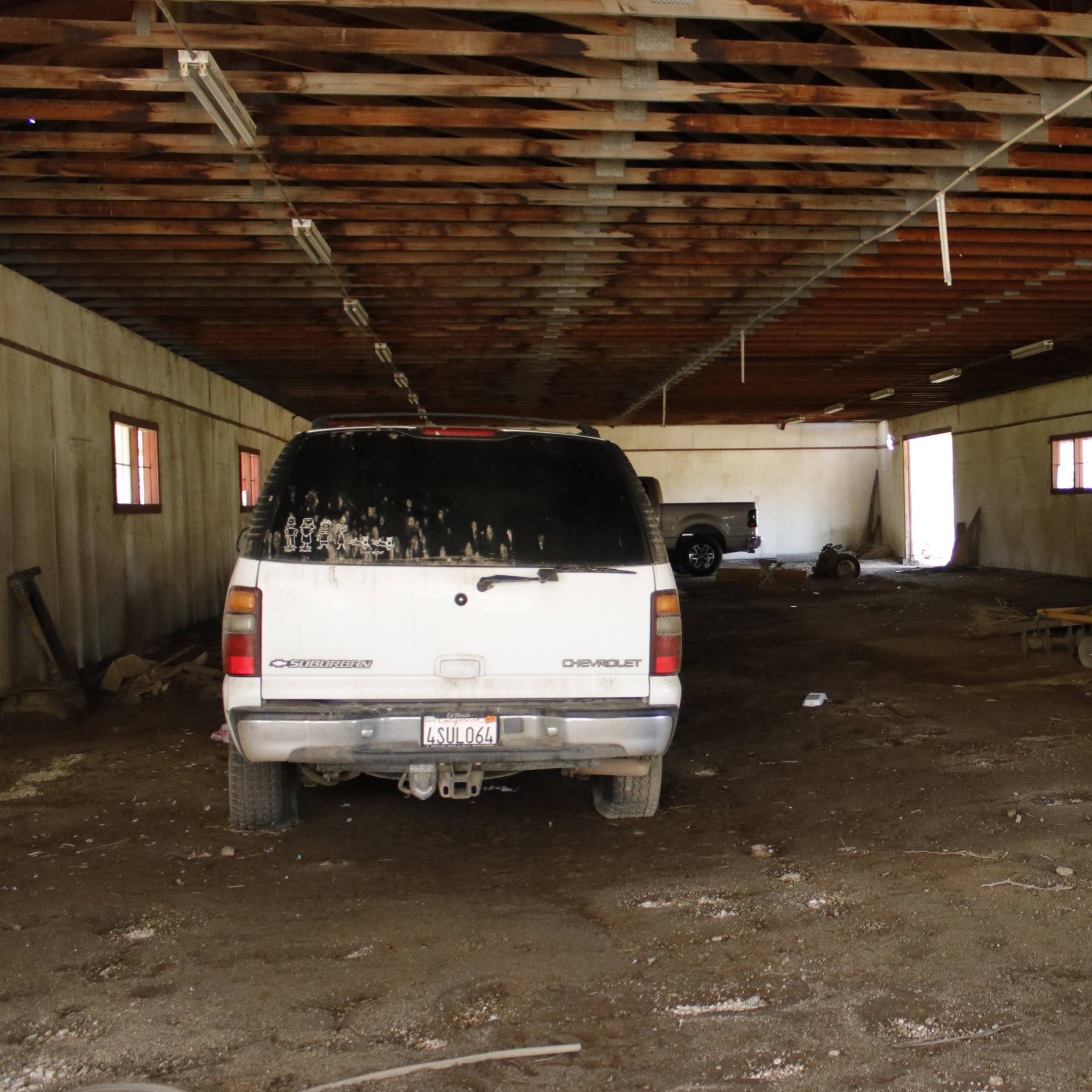 A spacious barn interior with two vehicles, a dirty Chevrolet SUV and a red tractor, situated on a dusty floor.