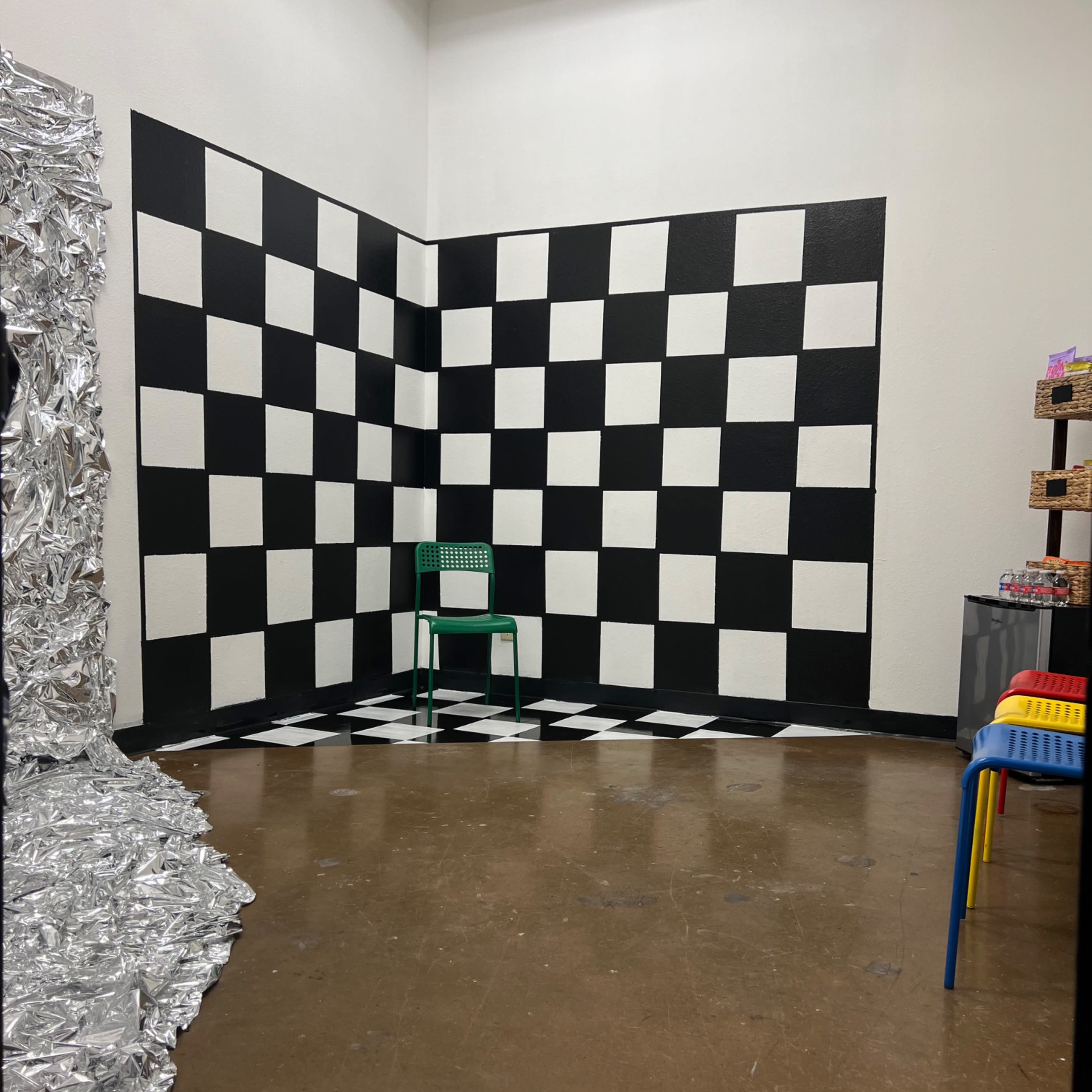 A room with a black and white checkered wall and floor, featuring a single green chair in the corner.