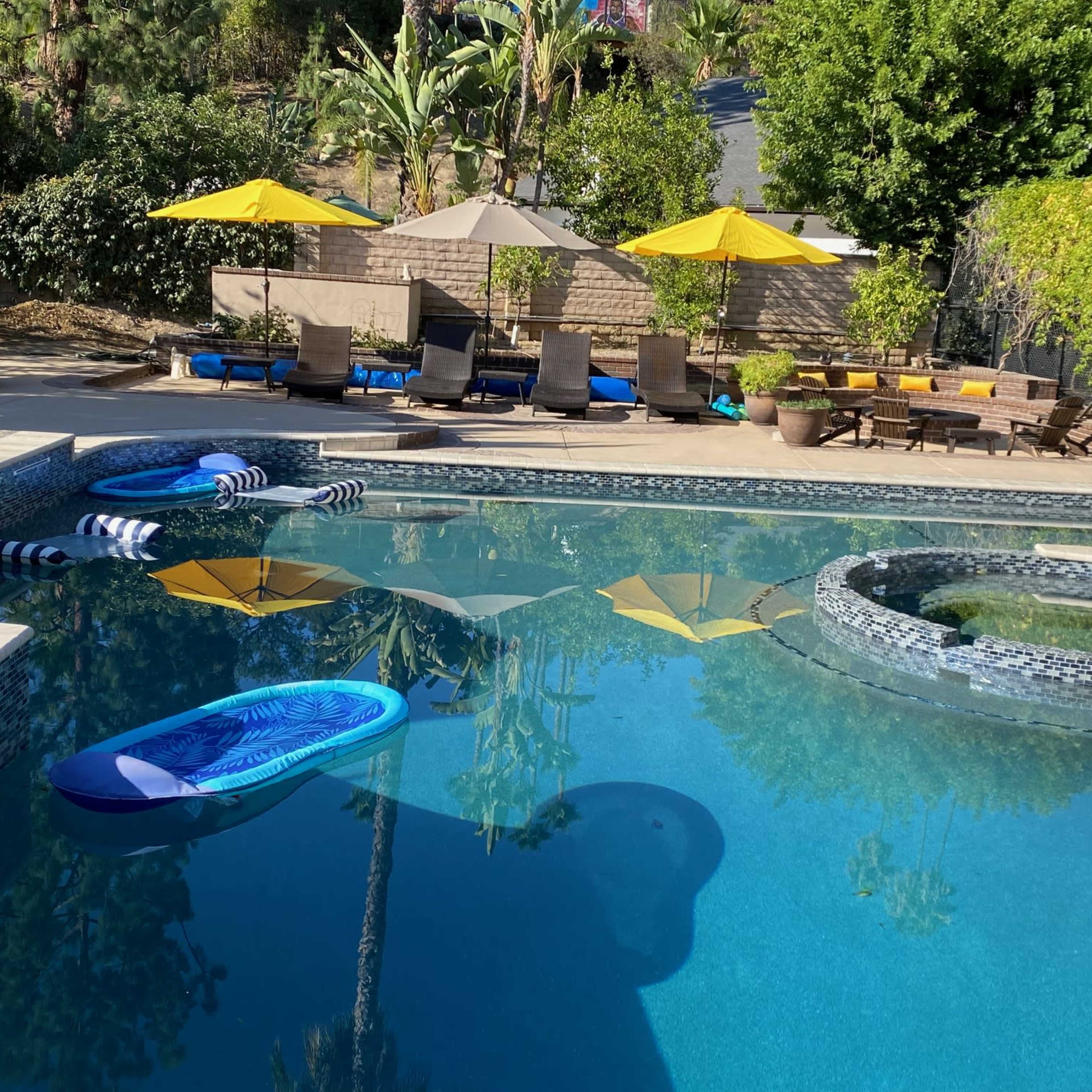 A swimming pool surrounded by yellow umbrellas, loungers, and inflatable floaties under clear blue skies.